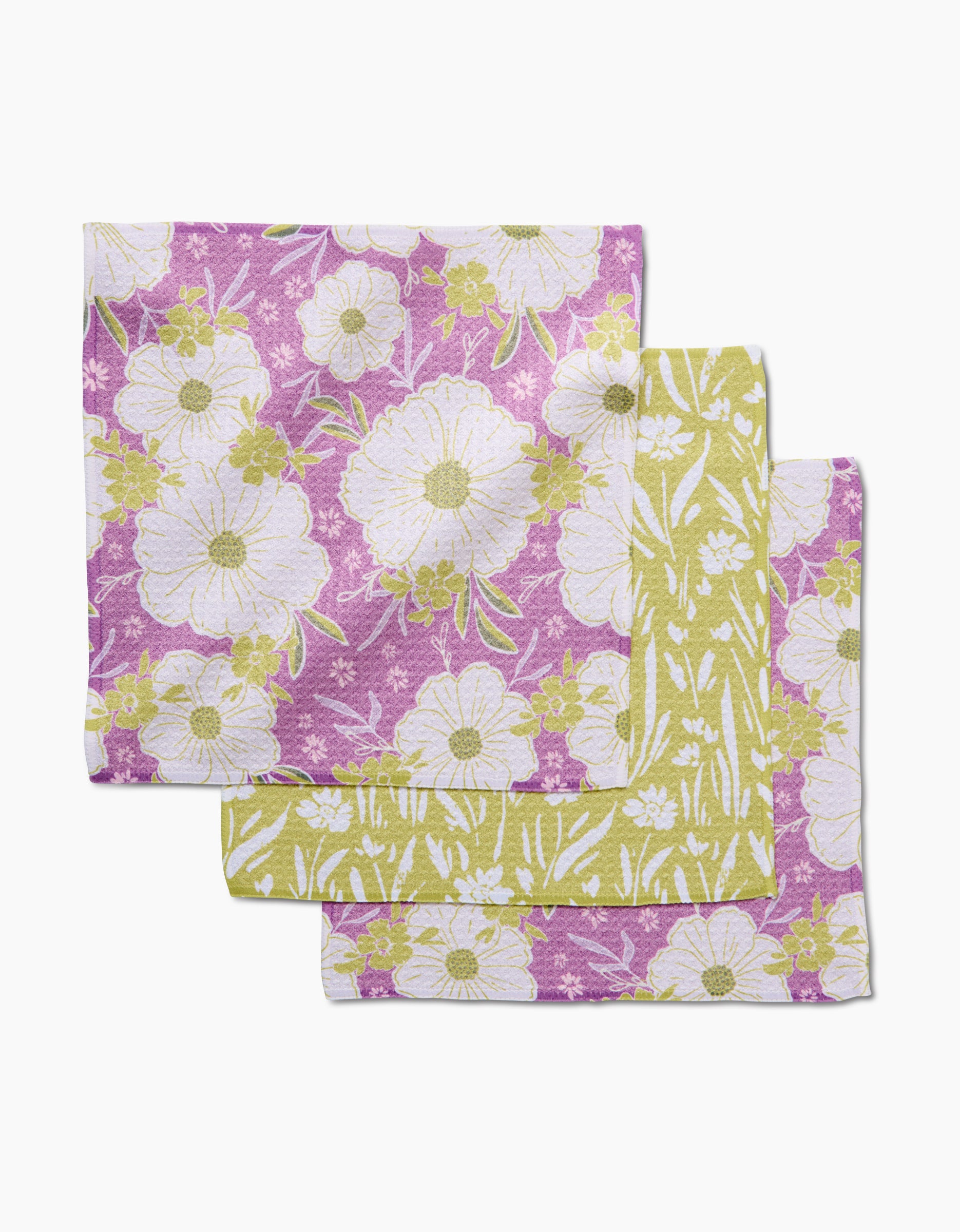 Two Ashley Celena “Field of Spring Flowers” Geoweave napkins—one purple, one light green, each with white and yellow floral prints—are displayed overlapping on a white background.
