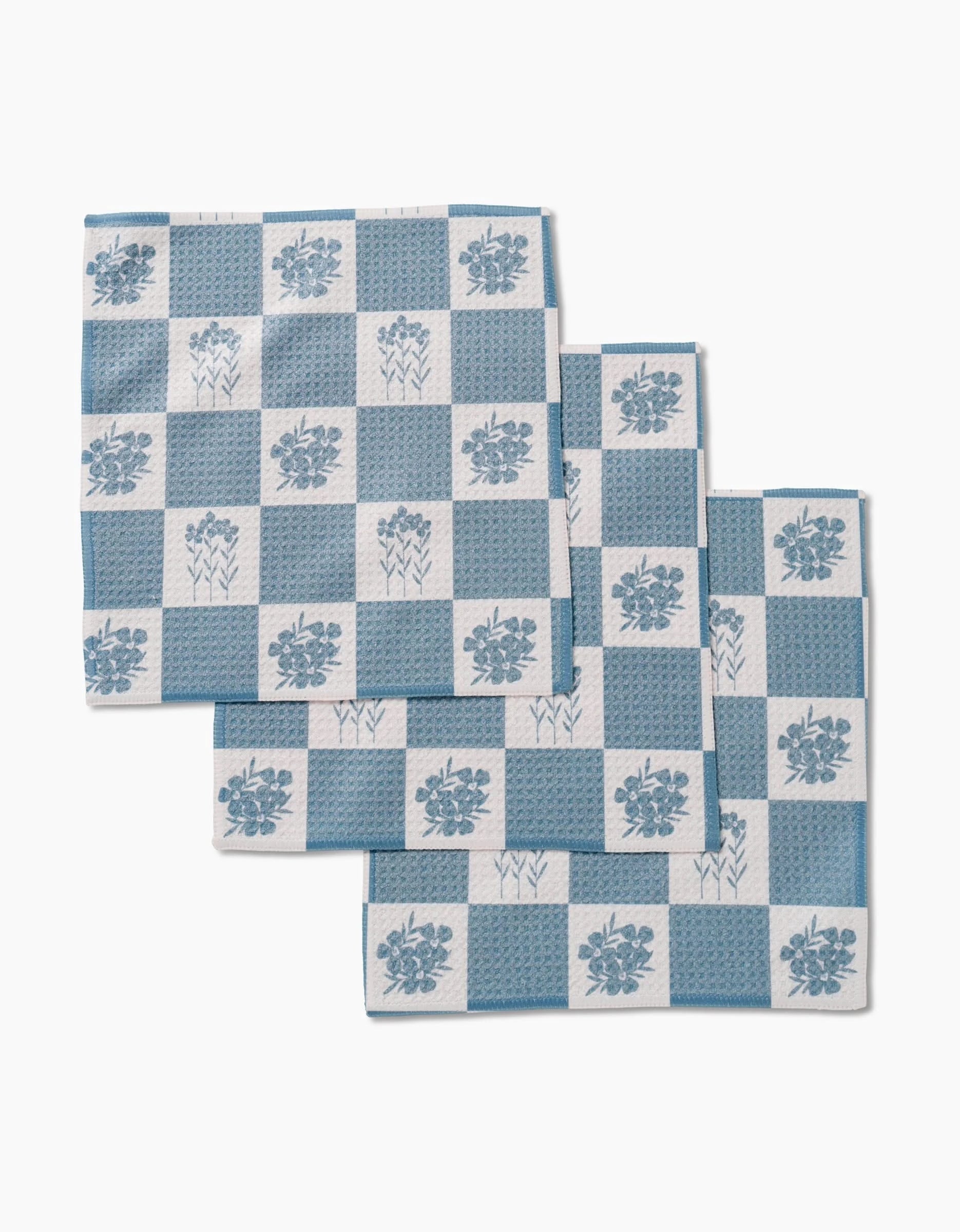 Three folded napkins from the Charlie Rowan Designs Floral Patchwork set, featuring blue and white checkered Geoweave fabric with floral and geometric patterns, are arranged overlapping on a white background.