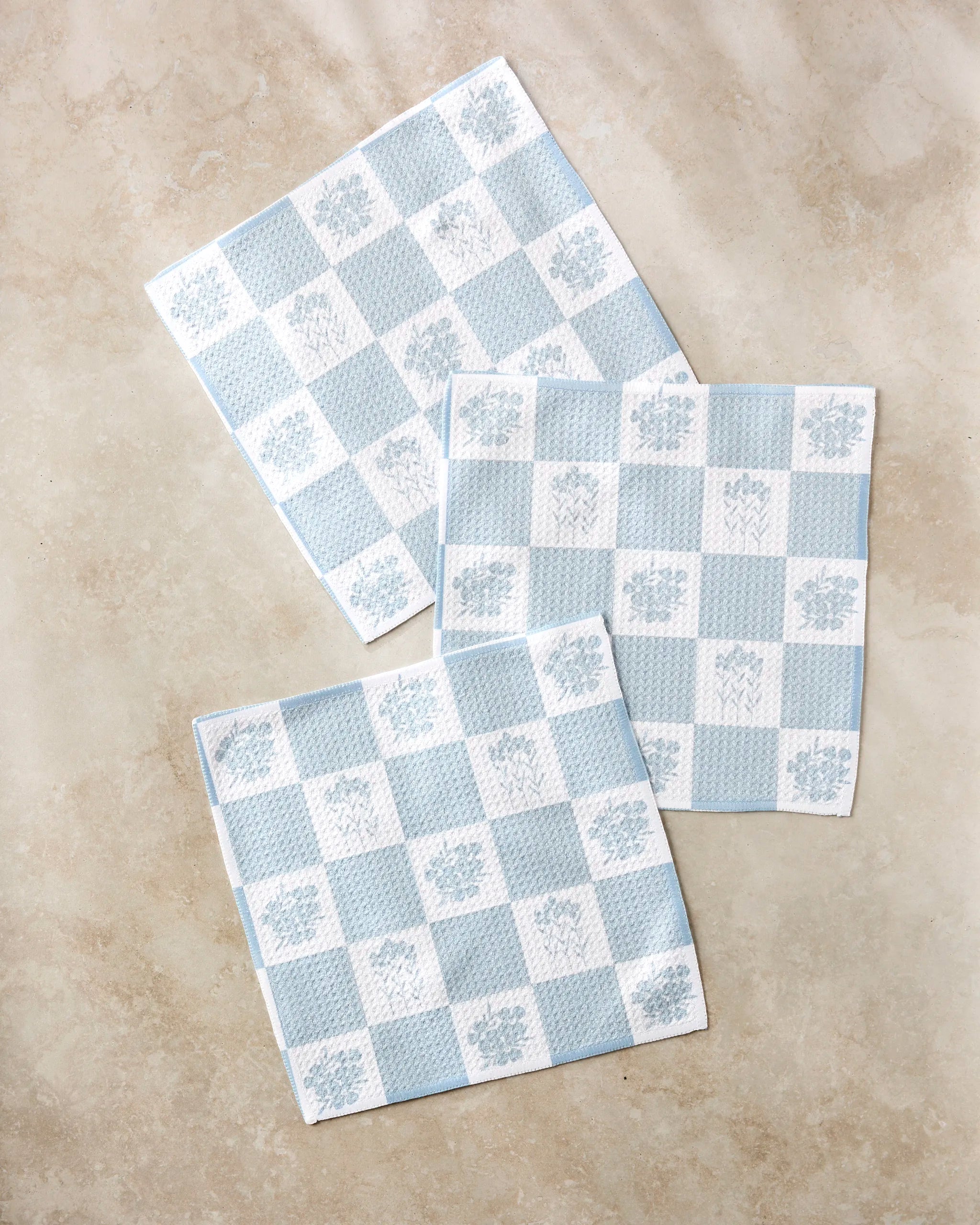 Three Floral Patchwork napkins by Charlie Rowan Designs, crafted from recycled materials, are arranged on a light beige surface.