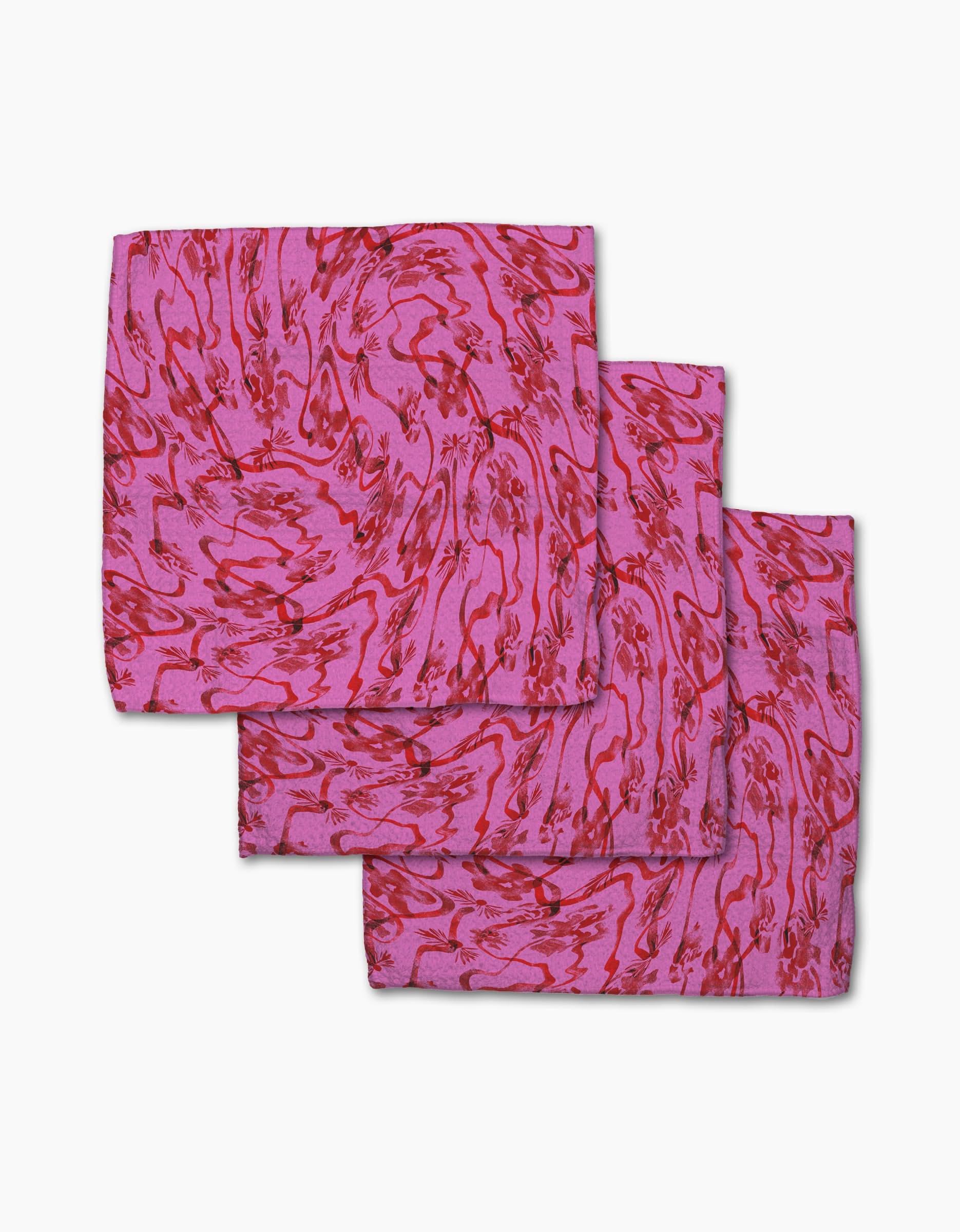 Three folded Geometry Floral Swirls Pink napkins made from Geoweave fabric, featuring a red abstract pattern, are arranged overlapping on a white background.