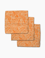 Three Florence napkins by Katie O’Shea, crafted from recycled materials, feature an intricate cream floral and leaf pattern on orange fabric and are shown overlapping on a white background.