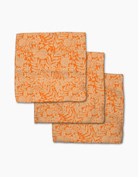 Three Florence napkins by Katie O’Shea, crafted from recycled materials, feature an intricate cream floral and leaf pattern on orange fabric and are shown overlapping on a white background.