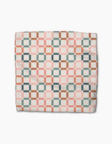 The Flower Patch quilt by Charlie Rowan Designs features interlocking pink, green, brown, and white squares in a geometric pattern on eco-friendly Geoweave fabric, displayed folded on a white background.