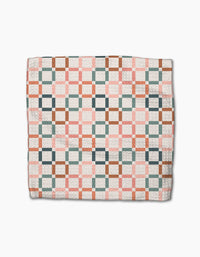 The Flower Patch quilt by Charlie Rowan Designs features interlocking pink, green, brown, and white squares in a geometric pattern on eco-friendly Geoweave fabric, displayed folded on a white background.