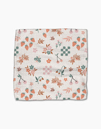 The Flower Patch dishcloth set by Charlie Rowan Designs features a folded eco-friendly Geoweave fabric with strawberries, cherries, bees, leaves, flowers, and green checkerboard patterns on a white background.