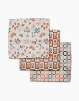 The Flower Patch Dishcloth Set by Charlie Rowan Designs features three eco-friendly Geoweave cloths, each with a unique pattern: strawberries and flowers, geometric leaves, and pink-teal-brown checks—all on a white background.