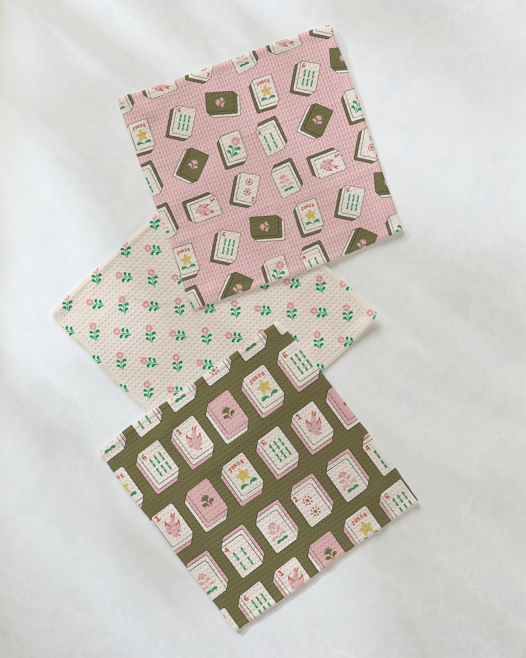 Three square fabric swatches with floral and seed packet patterns in pink, green, and brown tones are arranged diagonally on a white background, echoing the vibrant style of Geometry's Flower Tiles dishcloth set made from recycled materials.