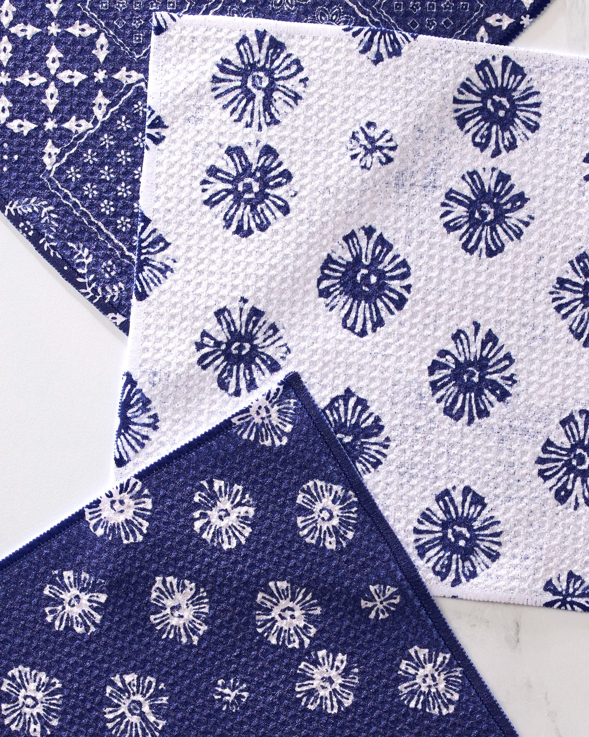 The Geometry Flowing Ocean dishcloth set includes four super-absorbent towels made from recycled materials, each featuring blue and white geometric flower patterns in alternating designs.