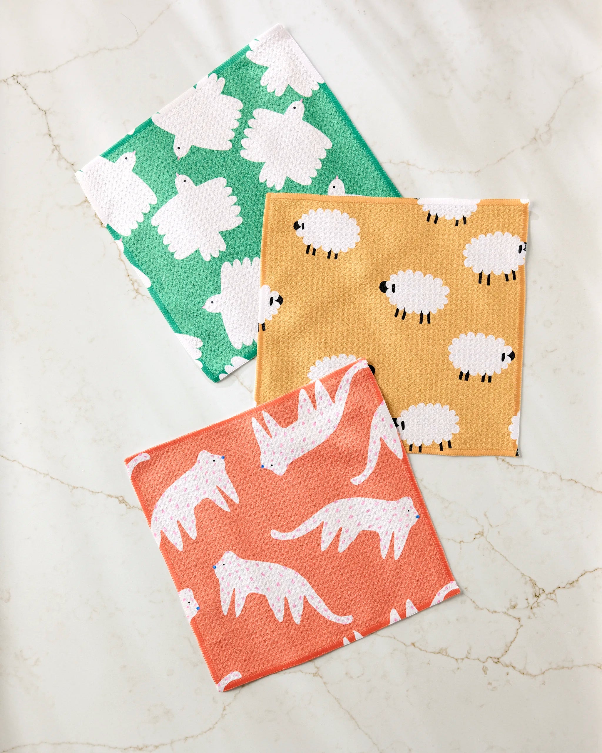 The Fluff and Feathers dishcloth set by Jennifer Bouron includes three super-absorbent, recycled dishtowels in green with sheep, yellow with small sheep, and orange with white tigers.