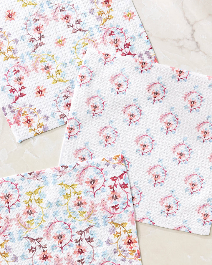 Three Folk Medallion paper napkins by Maayan Alper-Swan, each with unique pink, yellow, and blue floral patterns, are displayed on a marble surface—perfect for pairing with your favorite super-absorbent dishtowels.