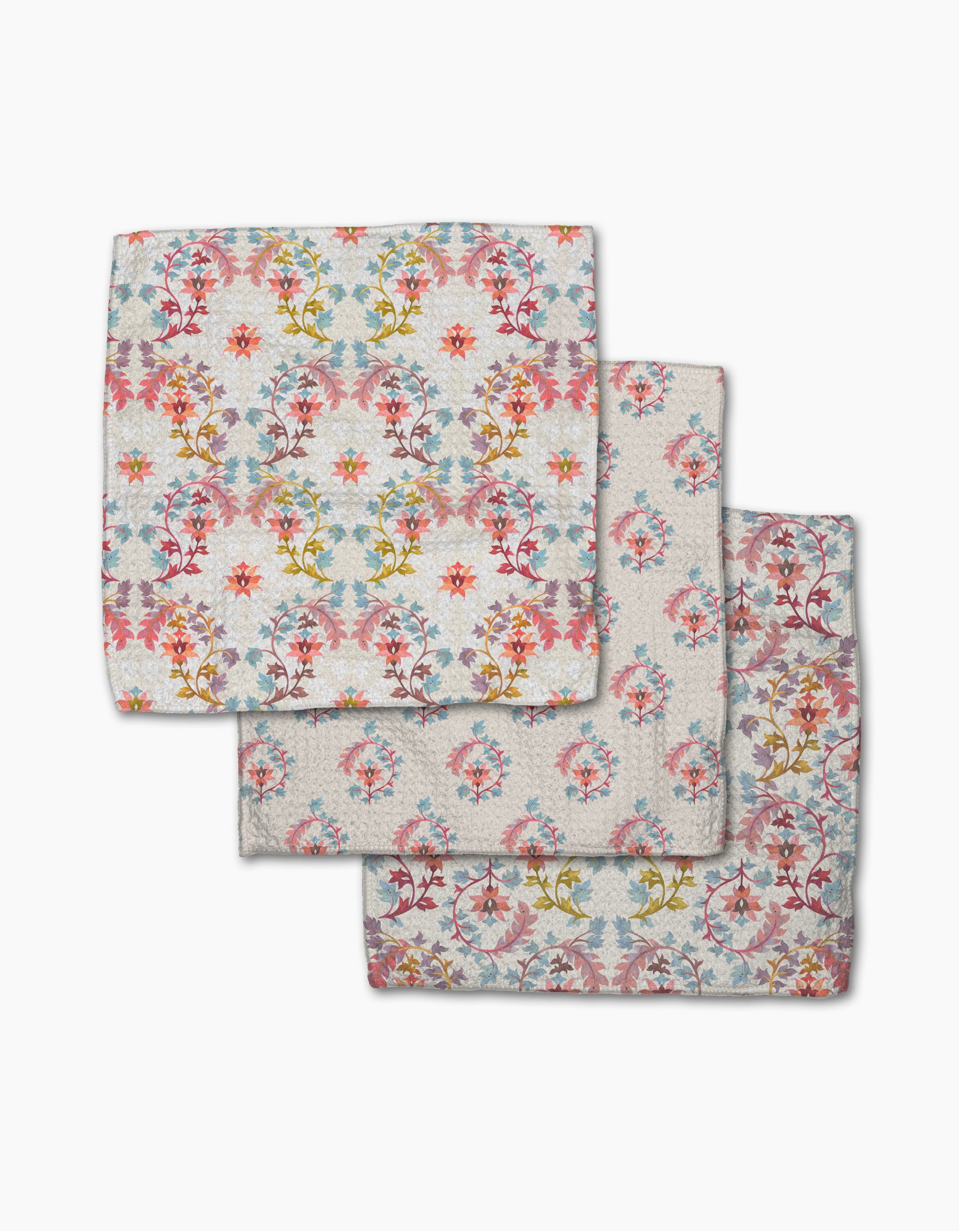 Three folded Folk Medallion cloth napkins by Maayan Alper-Swan, featuring a colorful floral pattern in pink, yellow, blue, and red on a light background, are stacked with slight overlap on a white surface.