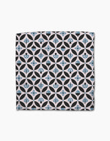 The Forest Findings dishcloth set by Anette Heiberg features square Geoweave fabric with geometric patterns—black circles, blue-tinted shapes, flowers, and abstract forms—on a light beige background.