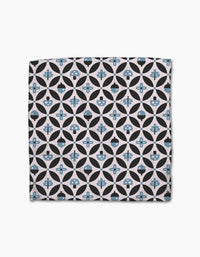The Forest Findings dishcloth set by Anette Heiberg features square Geoweave fabric with geometric patterns—black circles, blue-tinted shapes, flowers, and abstract forms—on a light beige background.