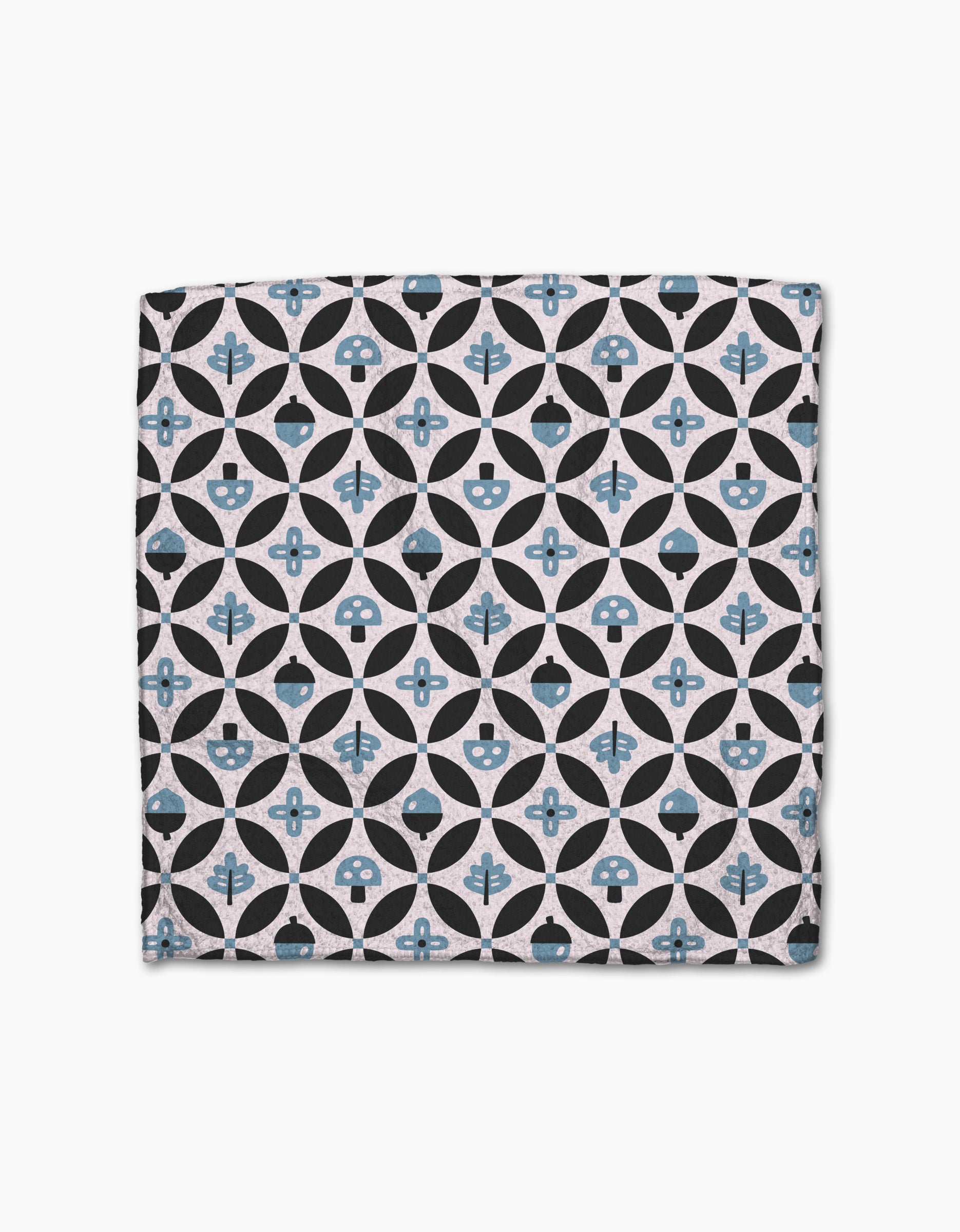 The Forest Findings dishcloth set by Anette Heiberg features square Geoweave fabric with geometric patterns—black circles, blue-tinted shapes, flowers, and abstract forms—on a light beige background.