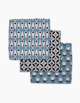 Three folded Anette Heiberg Forest Findings napkins—crafted from Geoweave fabric in blue, black, and white with unique geometric or floral patterns—are stacked with parts of each napkin visible.