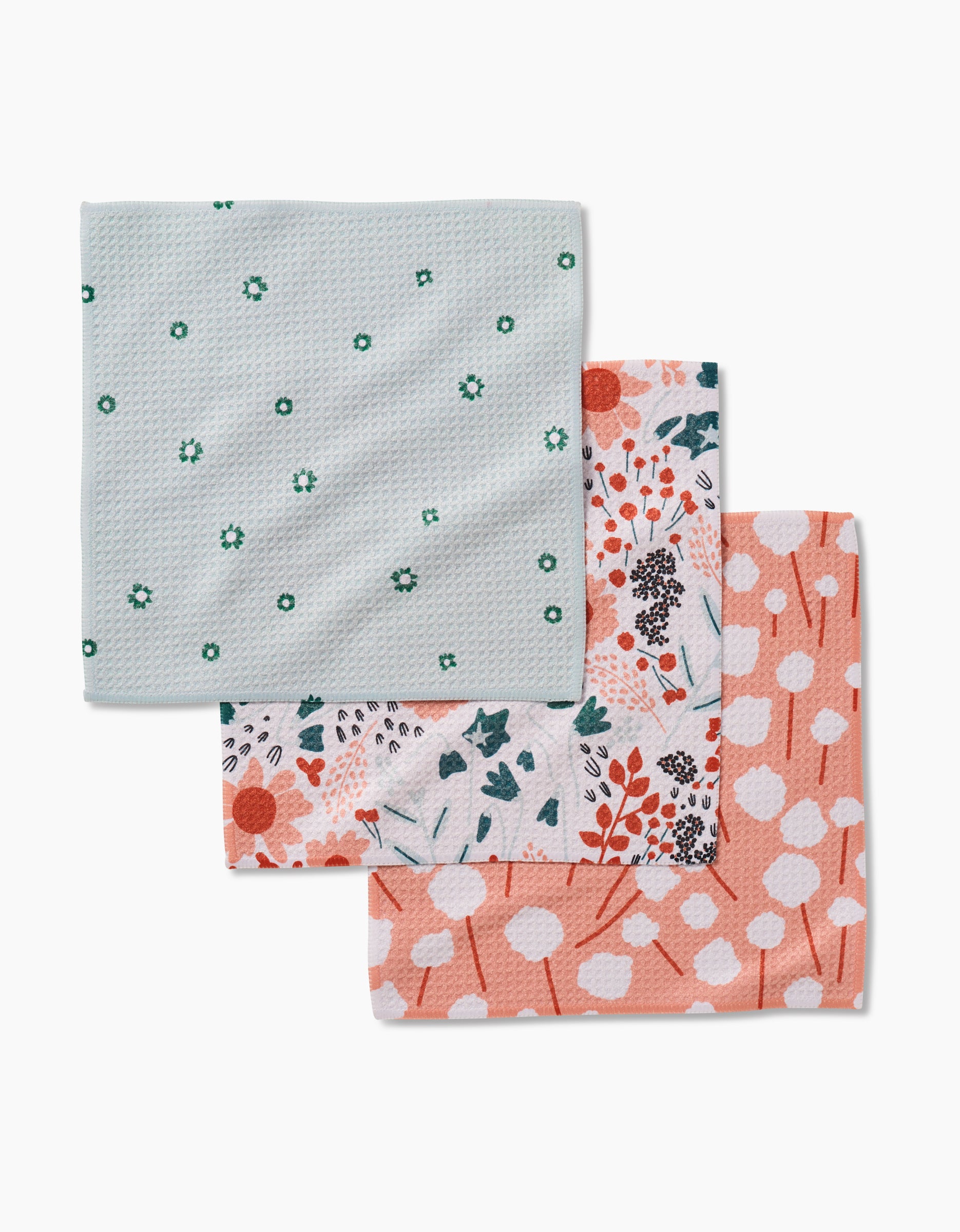 Coit Creative’s Forest Florals set includes three folded dishcloths made from recycled materials: light blue with green flowers, colorful floral print, and peach with white cotton spots.