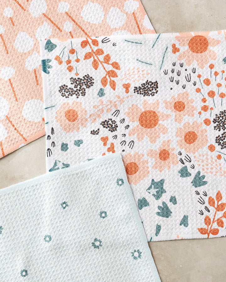 The Forest Florals dishcloth set by Coit Creative includes three super-absorbent dishtowels with abstract peach shapes, bold florals, and teal flowers, all made from recycled materials and shown on a light background.