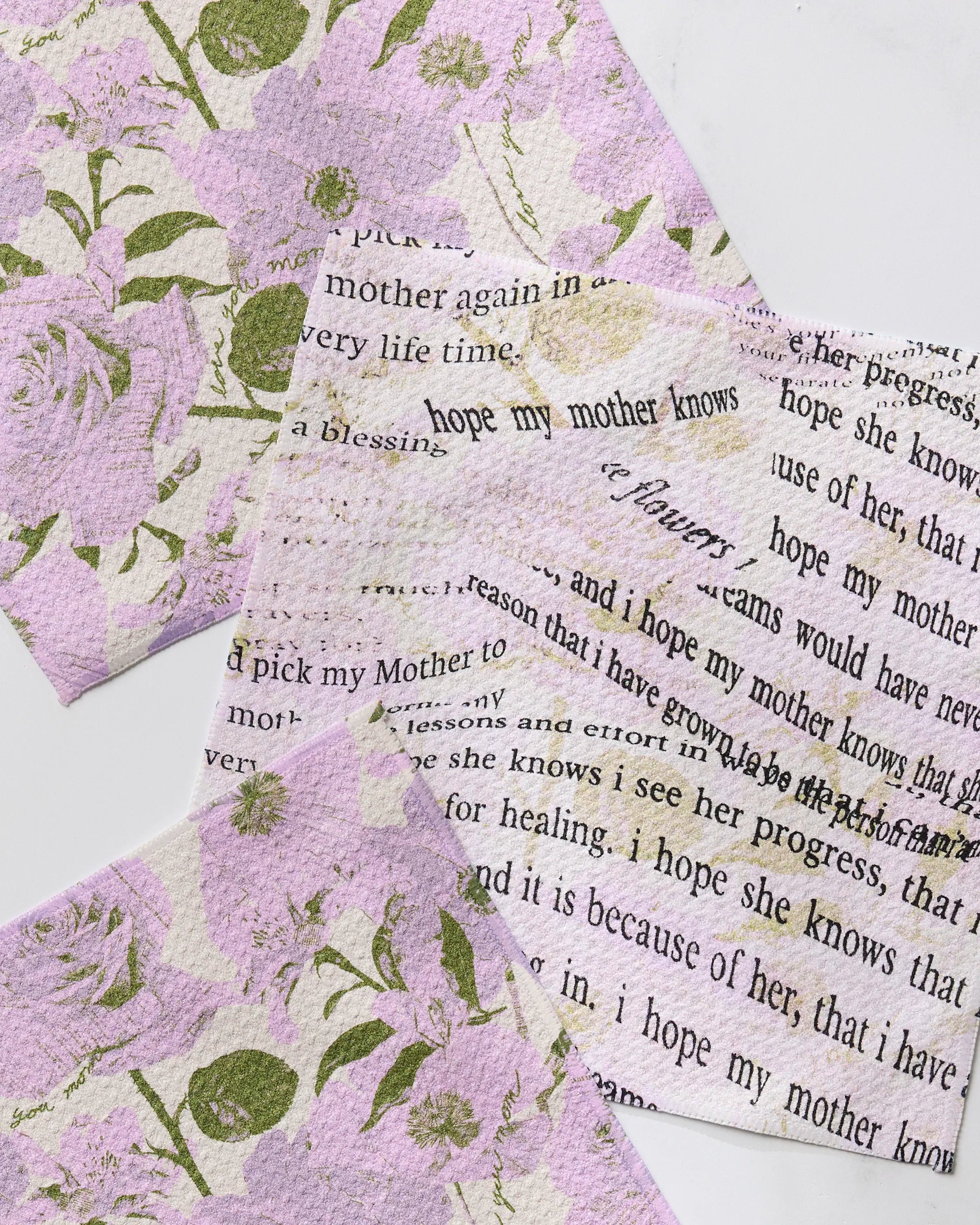 Three pieces of Geometry's Forever Mom recycled textured paper, featuring pastel pink and green floral designs—some with gratitude messages for moms—are displayed overlapping on a white surface.