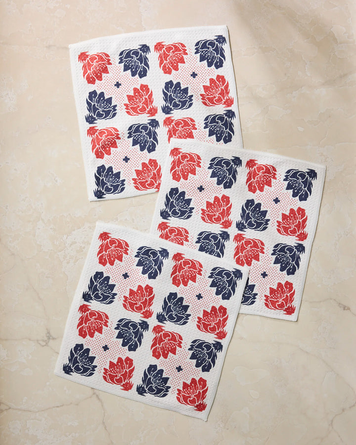 Three Founding Floral square napkins by Geometry, made from recycled material, display a red and navy blue floral pattern on a light beige marble surface.