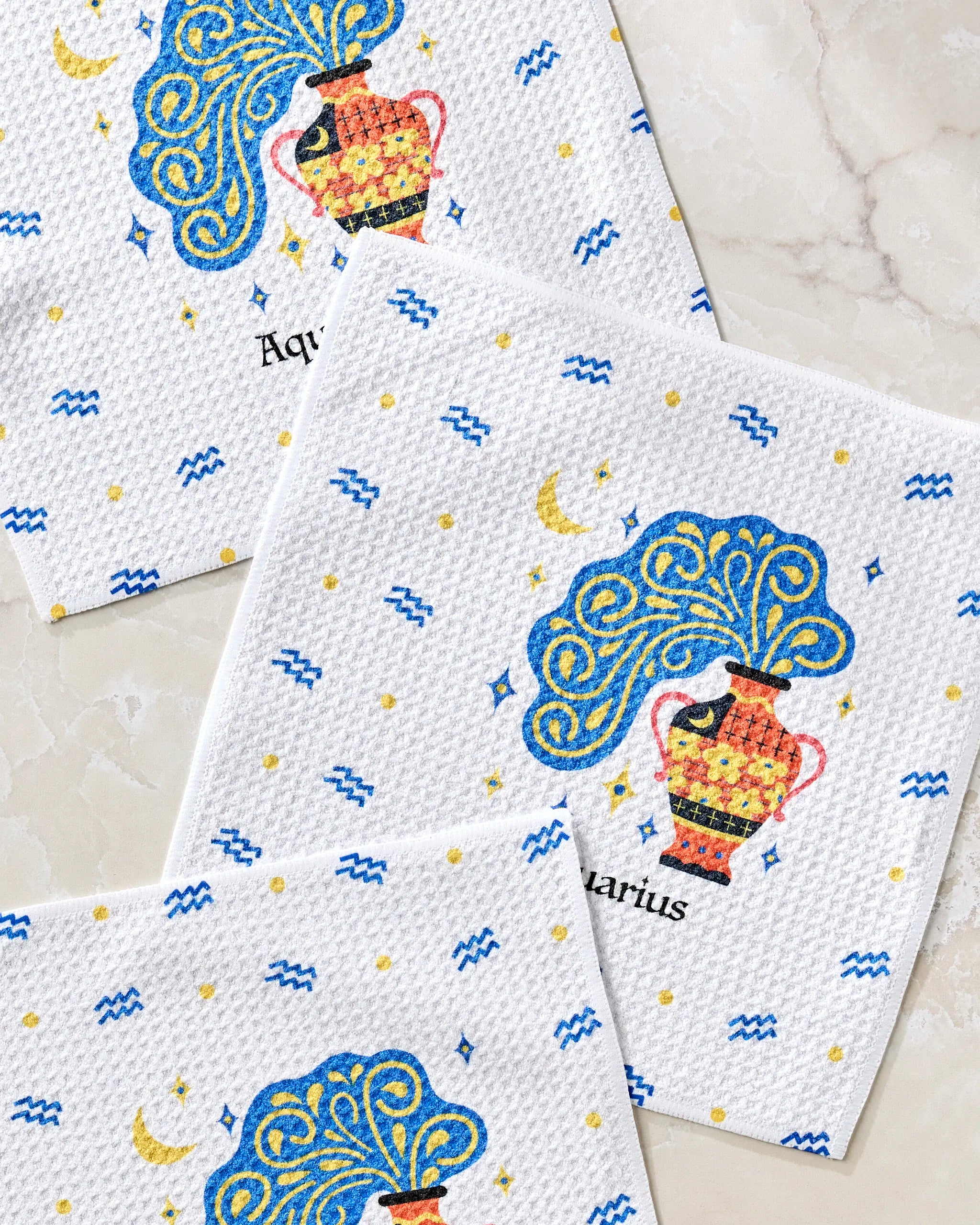 The Heather Zhou Free Aquarius set includes three white absorbent dishcloths, each featuring a colorful zodiac Aquarius design with a water jug, blue waves, yellow stars and moons, plus "Aquarius" written below.