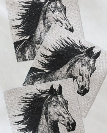 The Free Spirit dishtowel set by Geometry features three fabric squares with black and white horses and flowing manes on a light background, adding artistic charm and super absorbency to your kitchen.