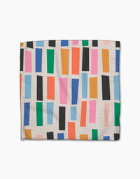 The Jennifer Bouron Fruit Basket Geoweave dishcloth features a textured white design with colorful, unevenly spaced vertical rectangles in green, blue, orange, pink, red, and black—made from recycled materials.