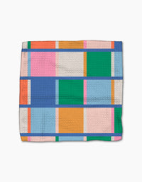 The Jennifer Bouron Fruit Basket blanket features a textured Geoweave and a geometric pattern of rectangles in blue, green, orange, pink, and peach, separated by thin blue lines on a white background.