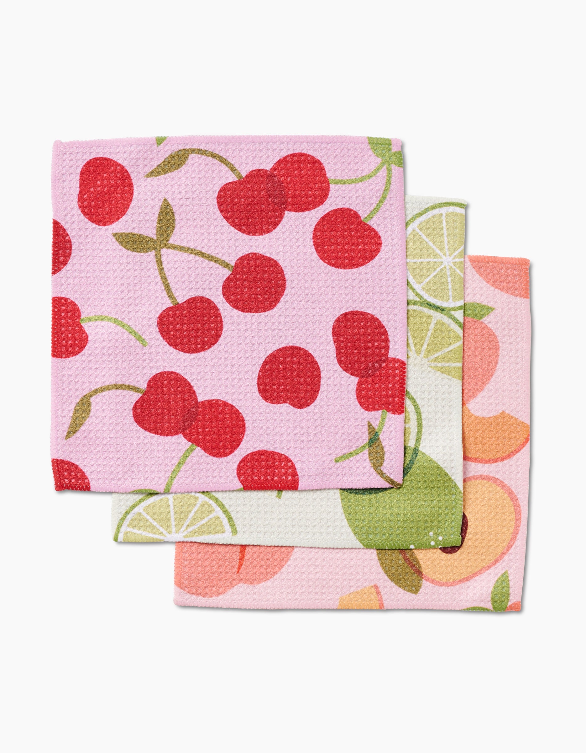 The GEOMETRY Fruit Fun set includes three durable Geoweave dishcloths with fruit patterns: cherries on pink, green limes on white, and orange and peach slices on light pink—perfect for any kitchen.