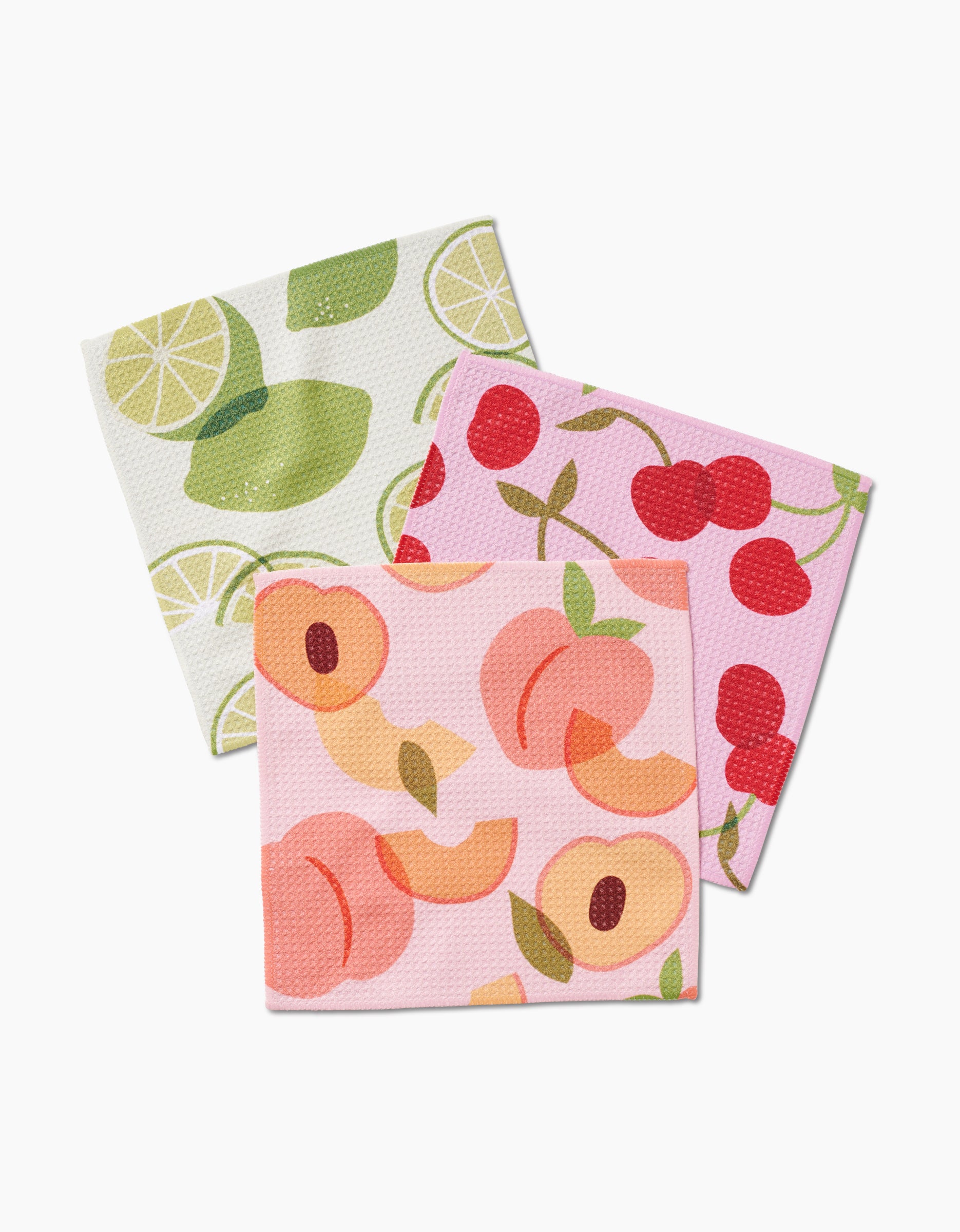 The GEOMETRY Fruit Fun set includes three rectangular dishcloths made from recycled materials, featuring playful fruit designs: limes, cherries on pink, and peach slices on light pink.
