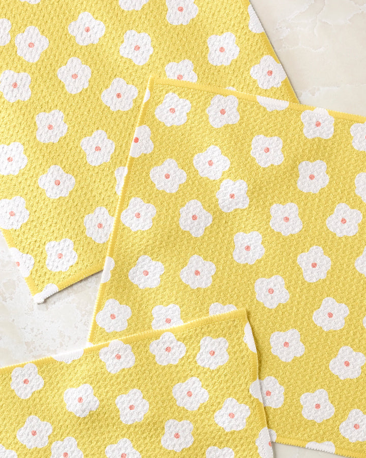 The Sara Mari Garden Crush dishcloth set includes three yellow, super-absorbent towels featuring white flowers with pink centers, all arranged against a light background.