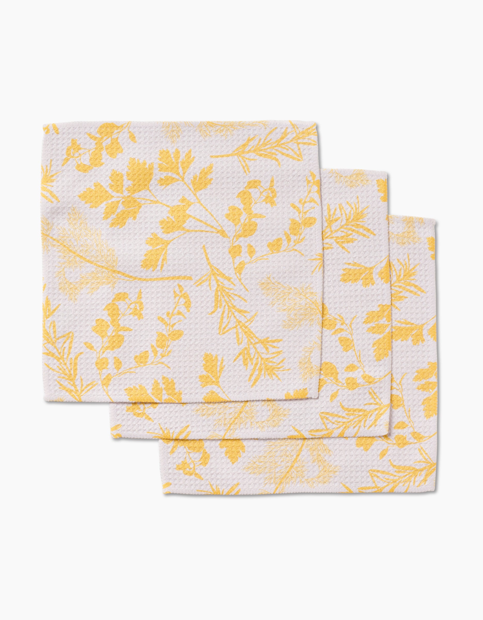 Three Garden of Gold napkins by GEOMETRY, made from Geoweave fabric and featuring a yellow floral pattern, are stacked in a staggered arrangement on a white background.