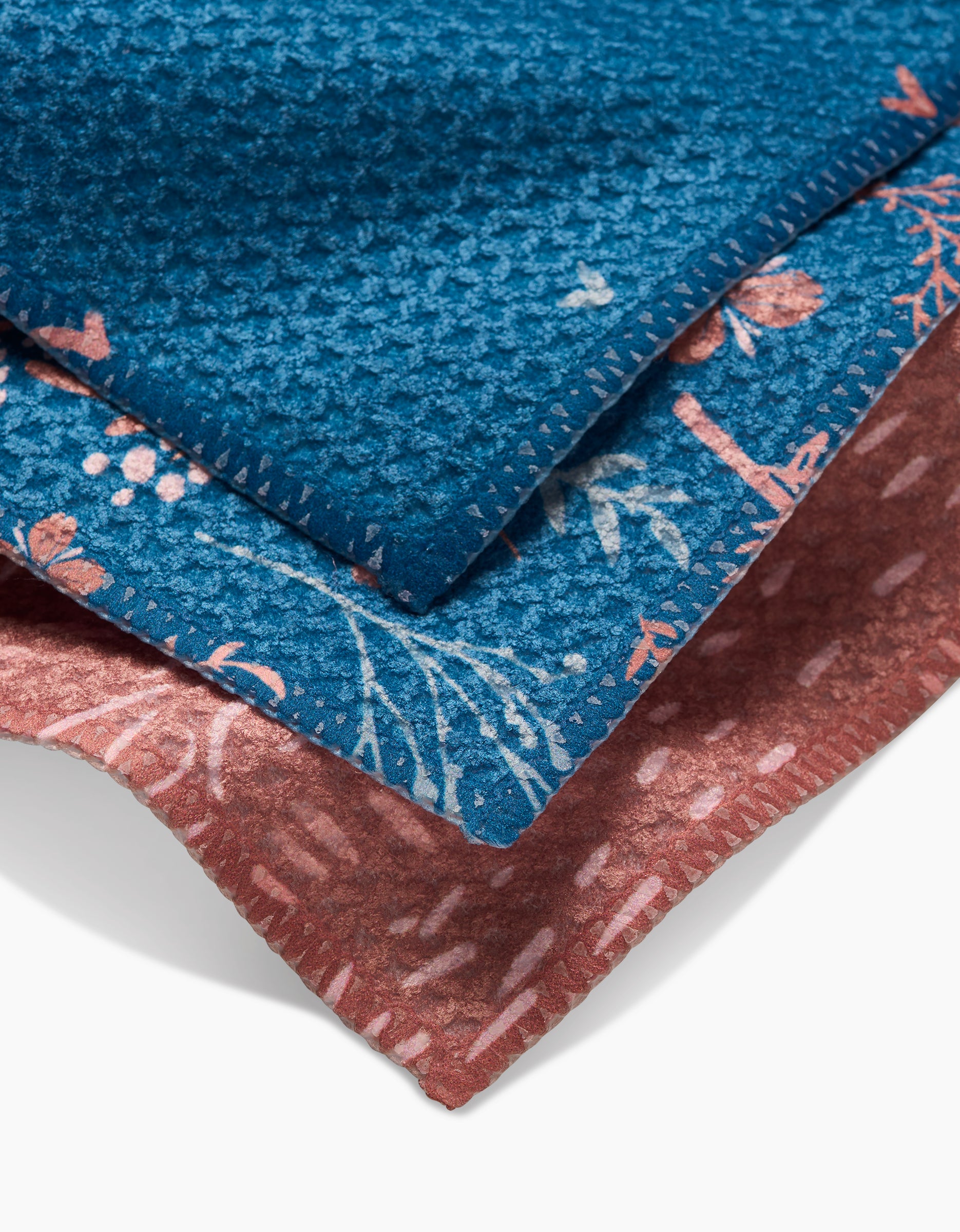A close-up of Garden Seeds by Danelys Sidron: three stacked seed packets—the top is solid blue, the middle features a blue floral pattern, and the bottom is pink with a subtle linear design.