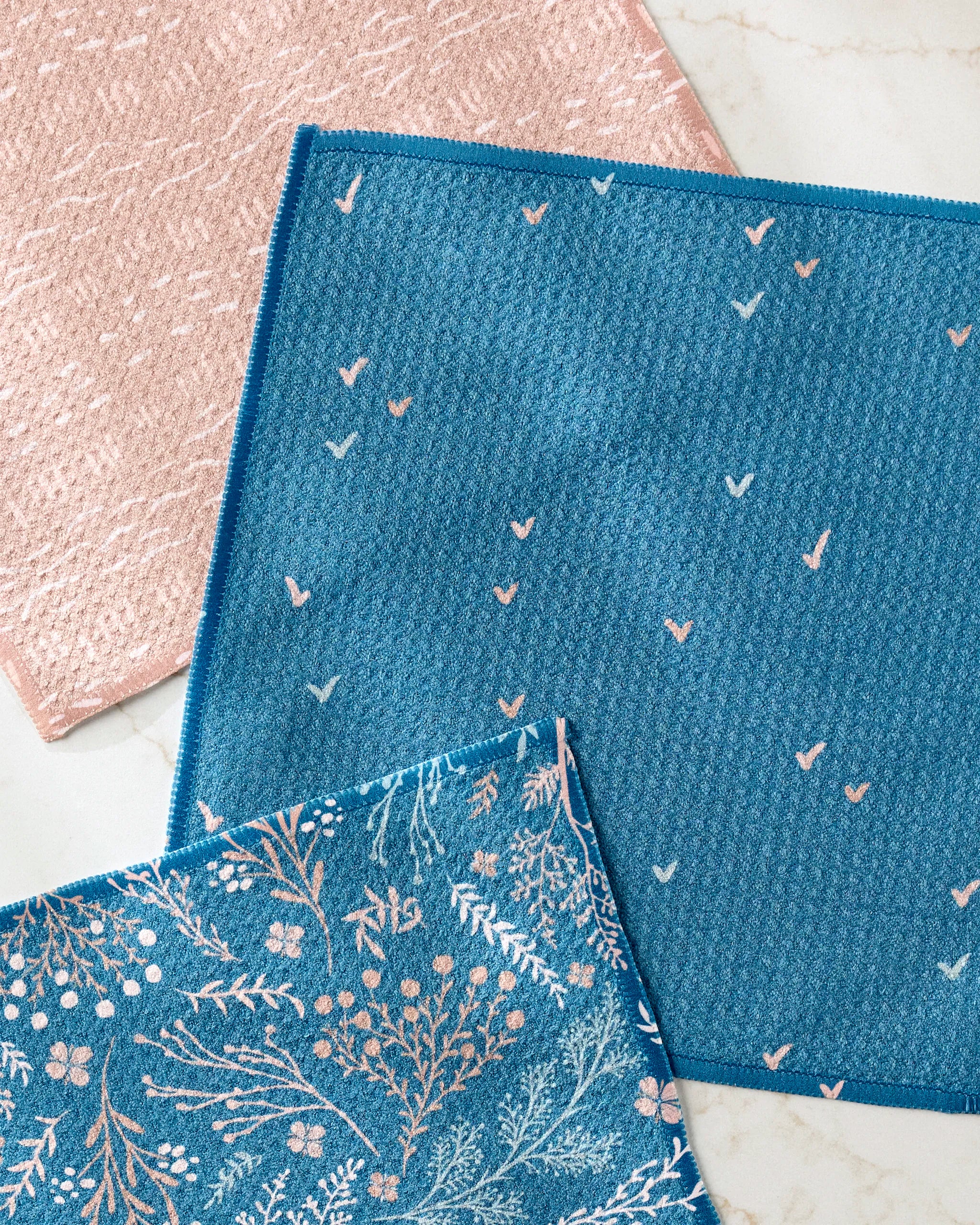 Three textured cloths from the Danelys Sidron Garden Seeds set are displayed on a light surface: one pale pink, one teal with heart-like patterns, and one teal with a floral print—all made from recycled materials.