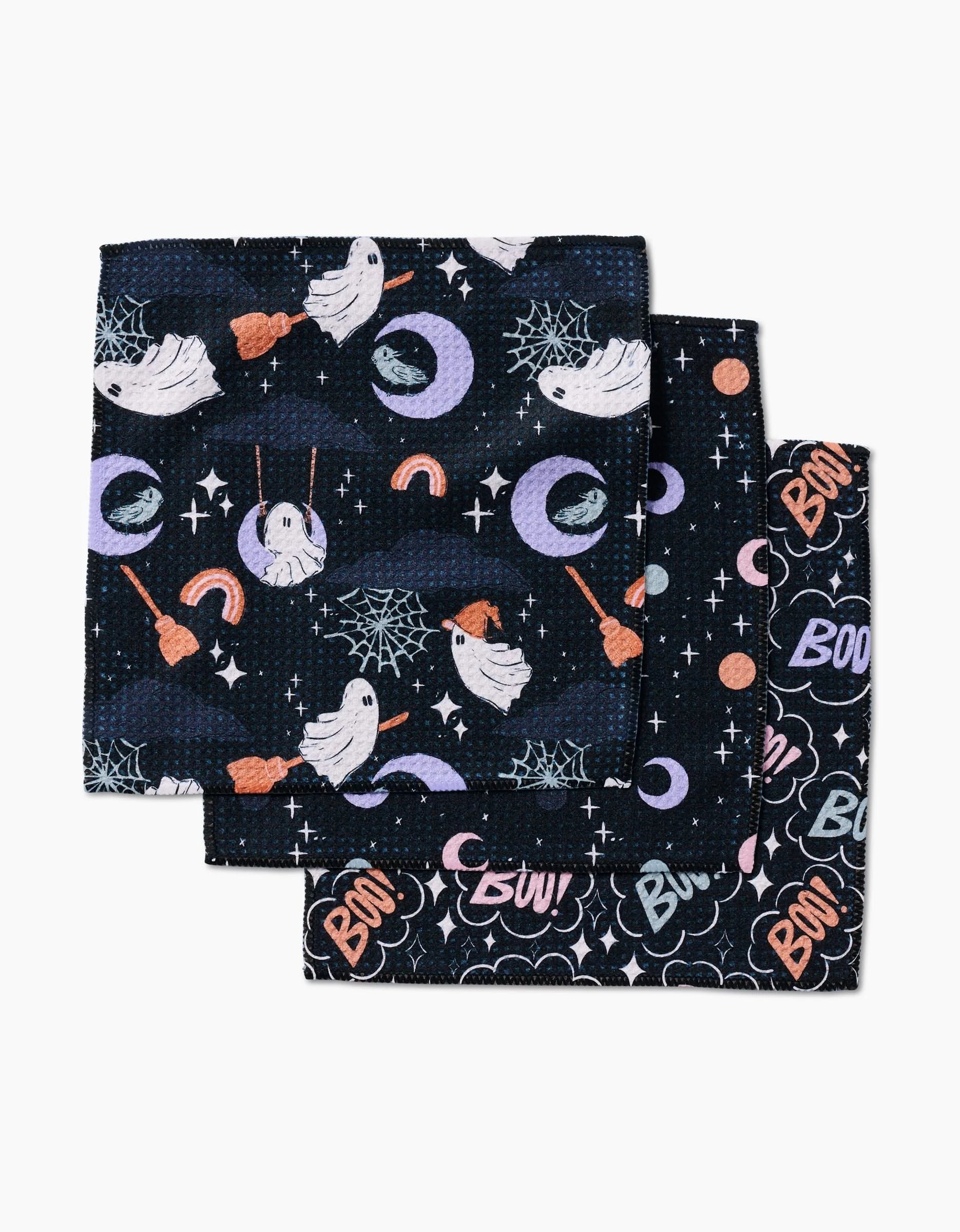 Charlie Rowan Designs Ghosts In The Night set includes three folded black napkins made from recycled materials, adorned with Halloween motifs—white ghosts, cobwebs, witches’ hats, moons, rainbows, and colorful Boo! text.