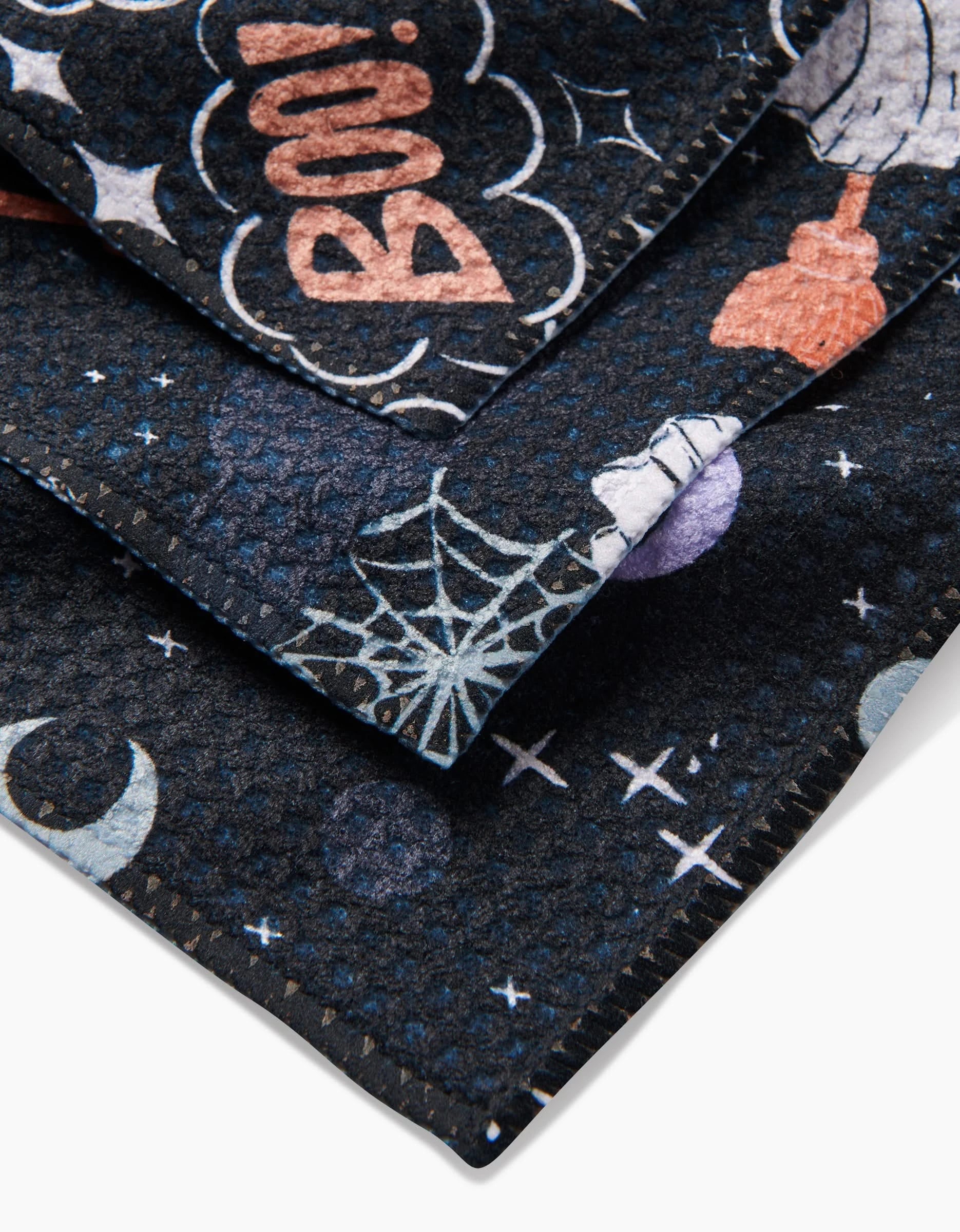 A close-up of the “Ghosts In The Night” Geoweave fabric by Charlie Rowan Designs, featuring Halloween prints like BOO!, a witch hat, spider webs, crescent moons, and stars in light blue, orange, and white.