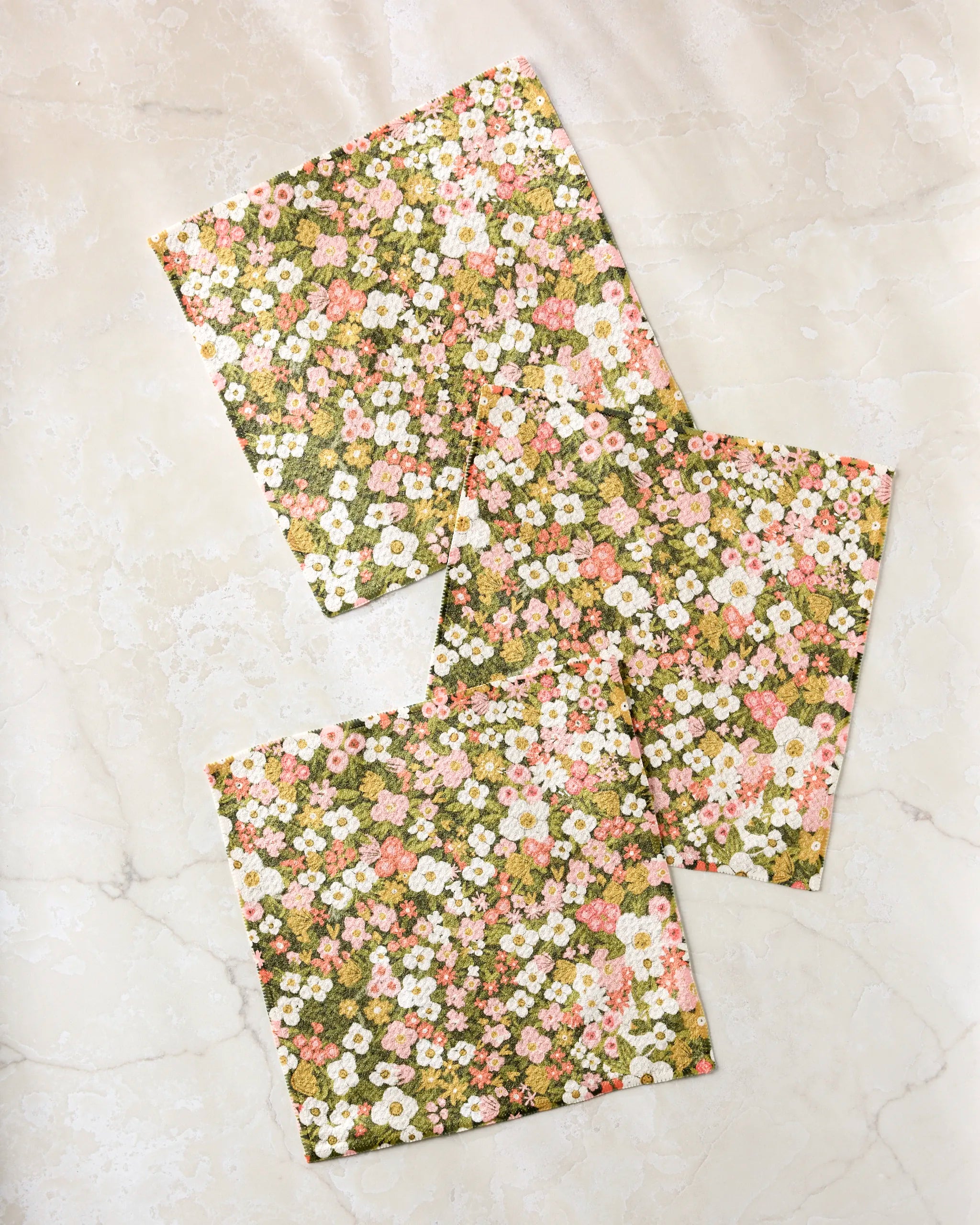 The Gilded Garden dishcloth set by Lisa Nelson includes three rectangular pieces made from recycled fabric, featuring a delicate floral pattern in white, pink, and green—perfect as super-absorbent kitchen cloths.