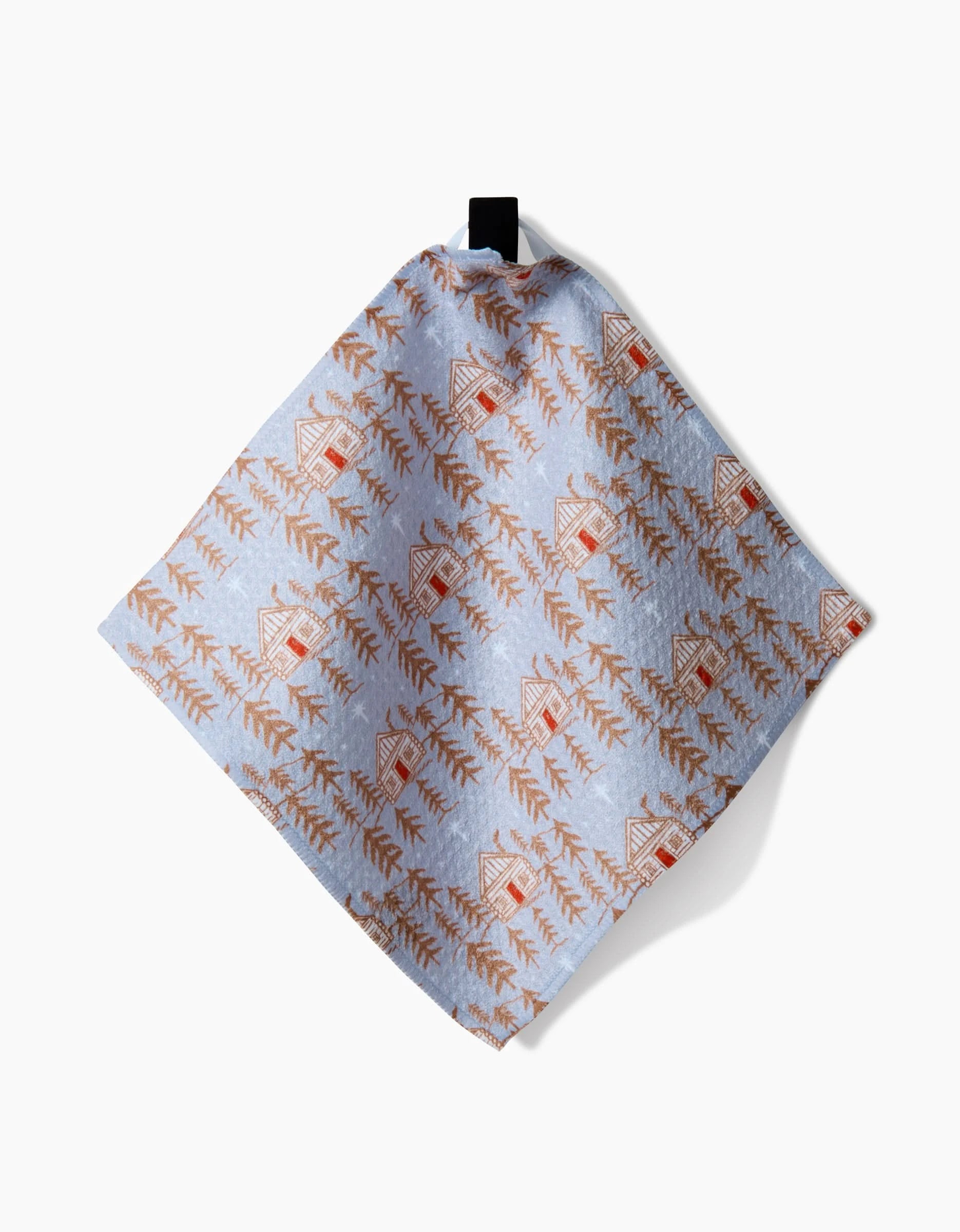The Gingerbread Homestead tea towel by Roxy Marj features brown houses and pine trees on light blue Geoweave fabric, hanging from a black loop against a white background.