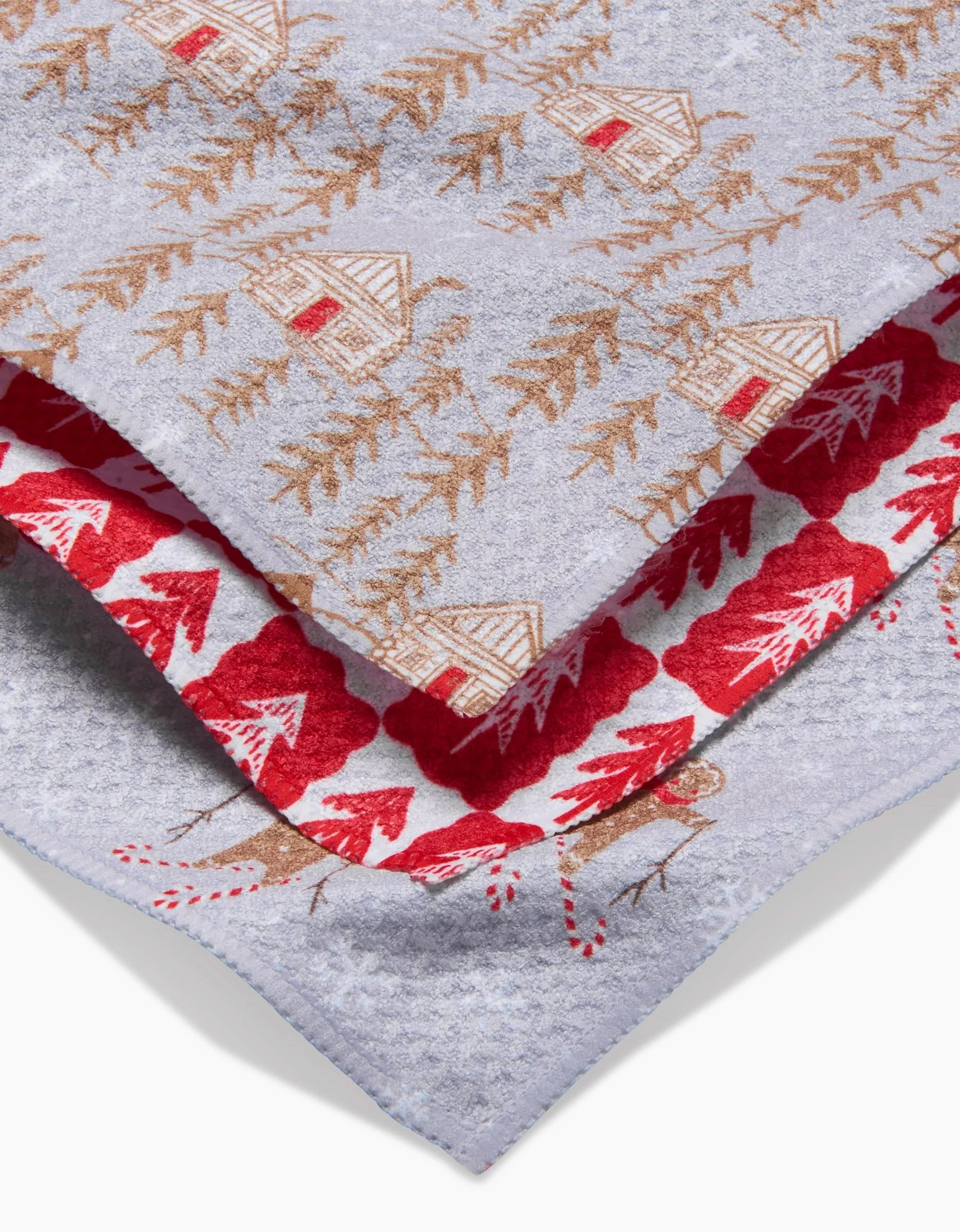 A close-up of Roxy Marj’s Gingerbread Homestead dishcloth set: one with brown cabins and trees on grey, the other with red leaves and a brown reindeer on white—perfect kitchen tea towels for any home.