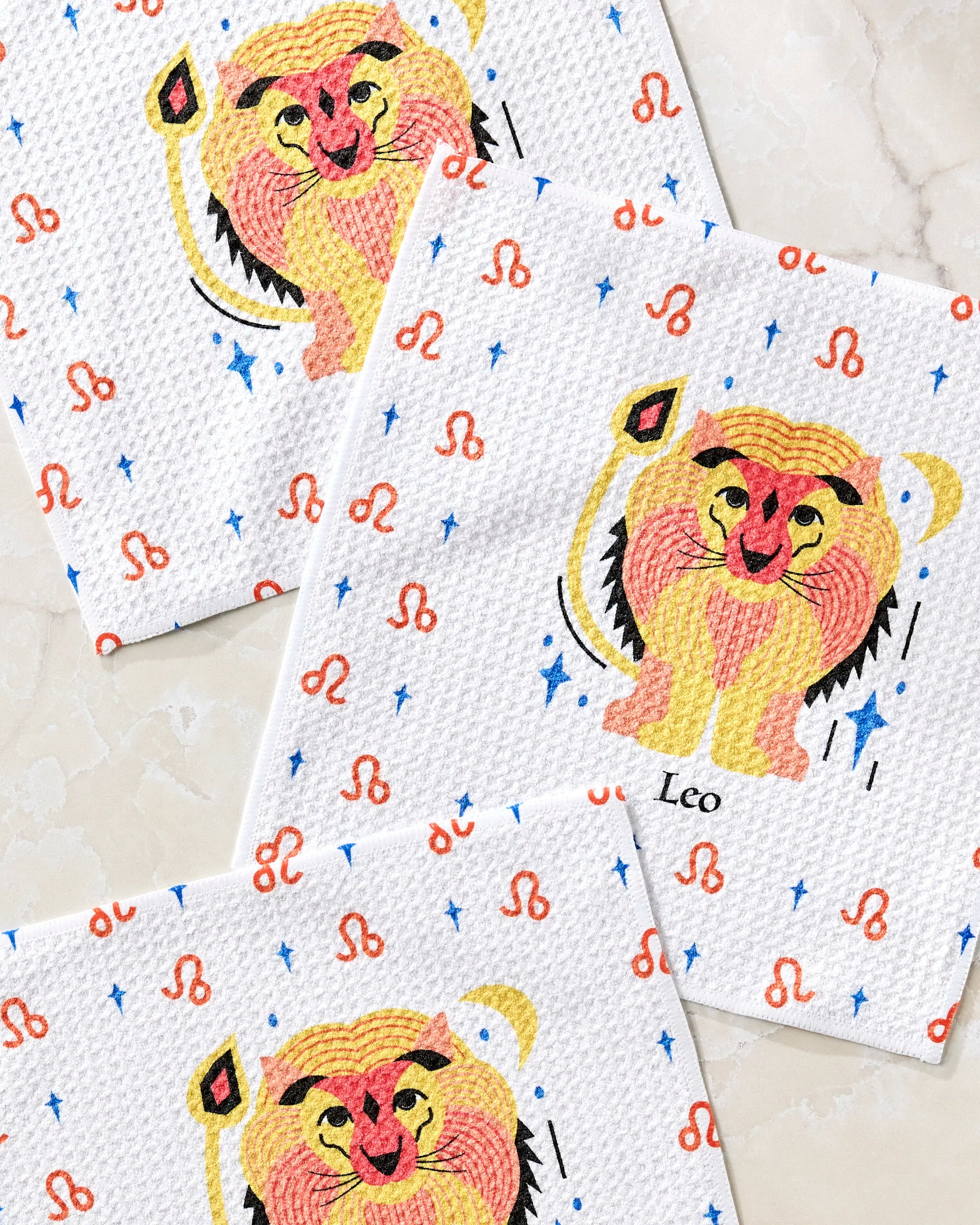 The Glowing Leo paper napkins by Heather Zhou feature colorful lion illustrations with orange zodiac symbols and blue stars on a white textured background—ideal for pairing with eco-friendly towels in your zodiac-themed decor.