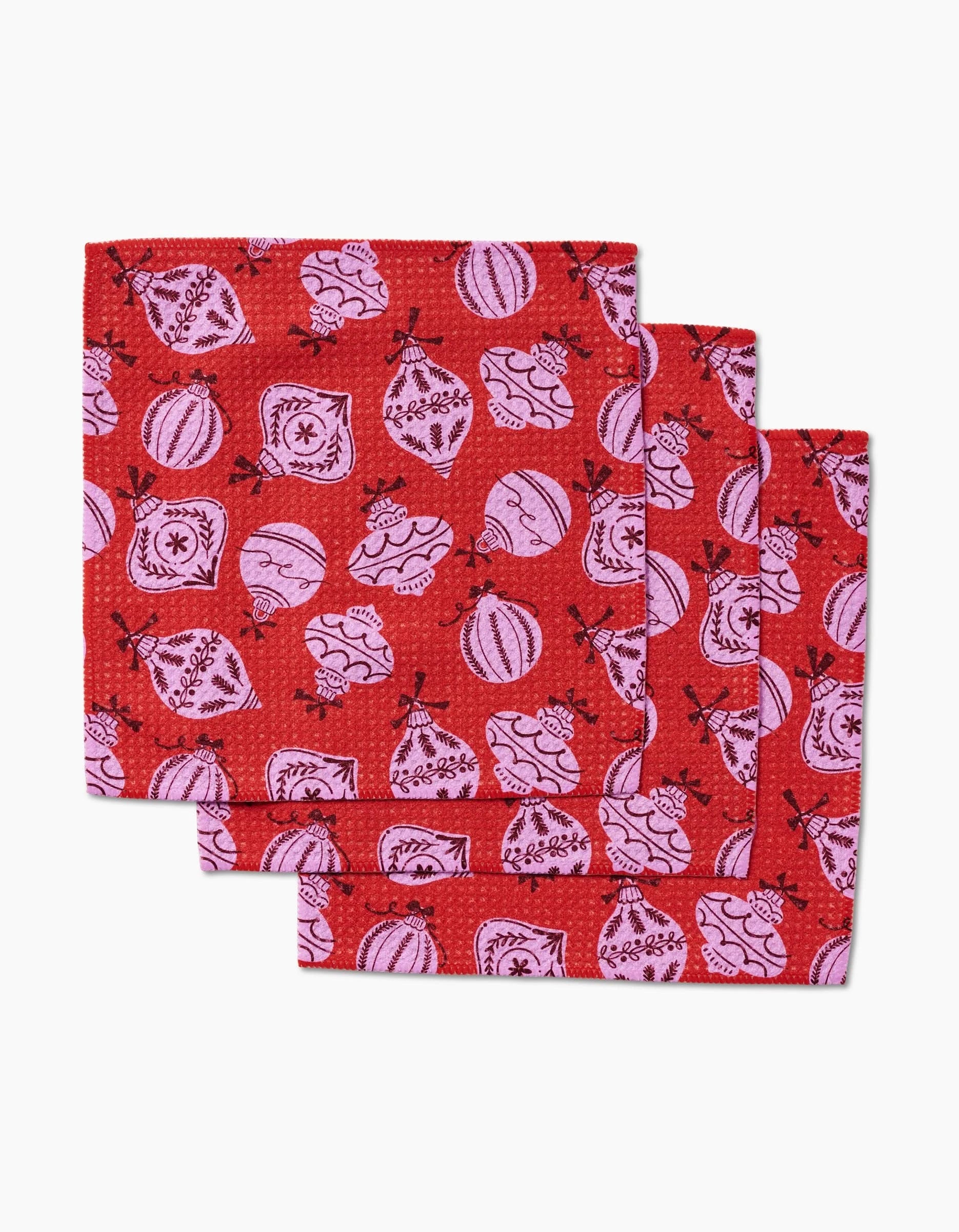 Three red Grams Ornaments dishcloths by Charlie Rowan Designs feature pink Christmas ornament patterns. Crafted from durable Geoweave fabric, they are neatly stacked and slightly offset to showcase their festive style.