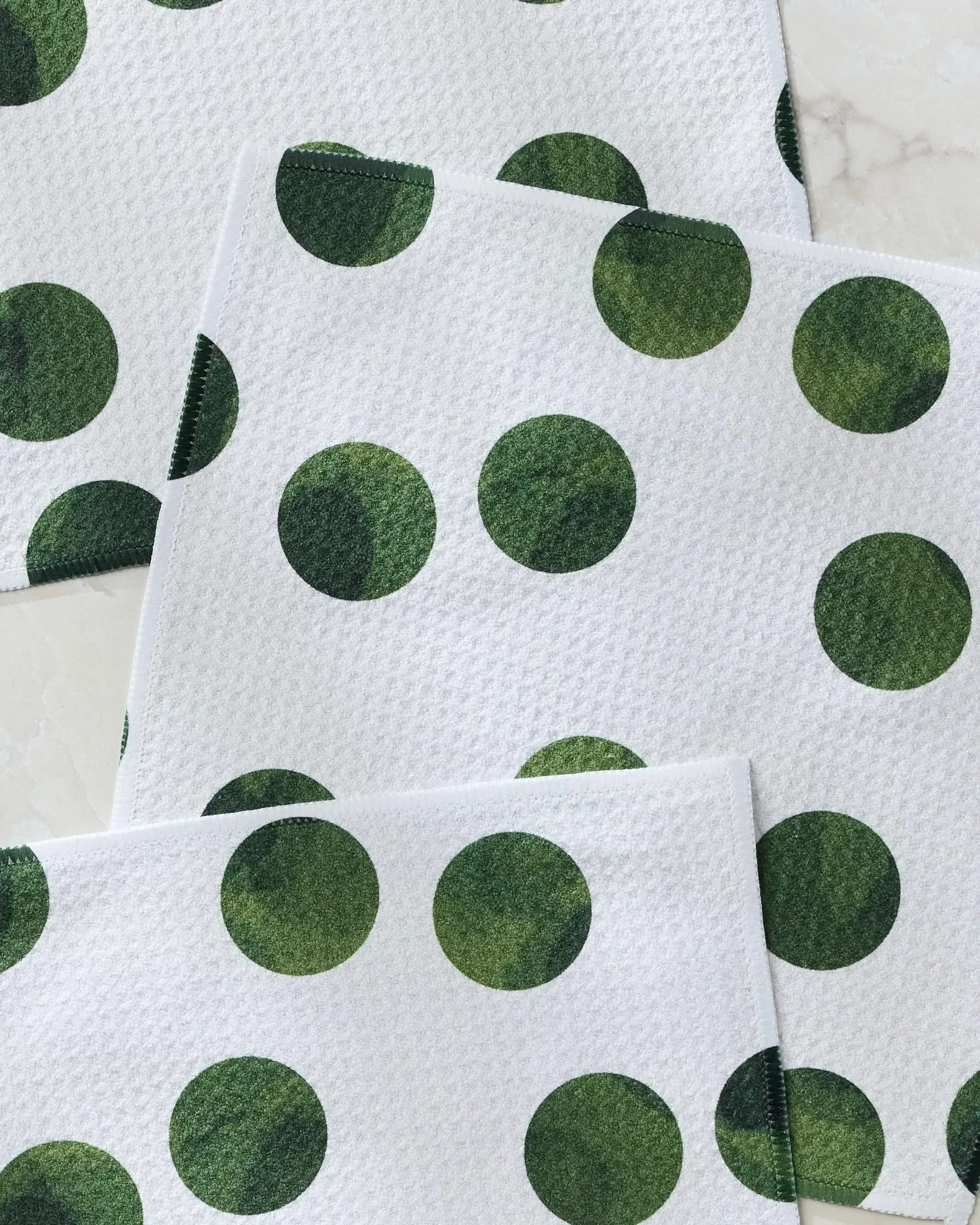 Geometry's Grass Polka napkins, made from recycled materials, feature large dark green polka dots on white and are arranged overlapping on a light surface for an eco-friendly touch.