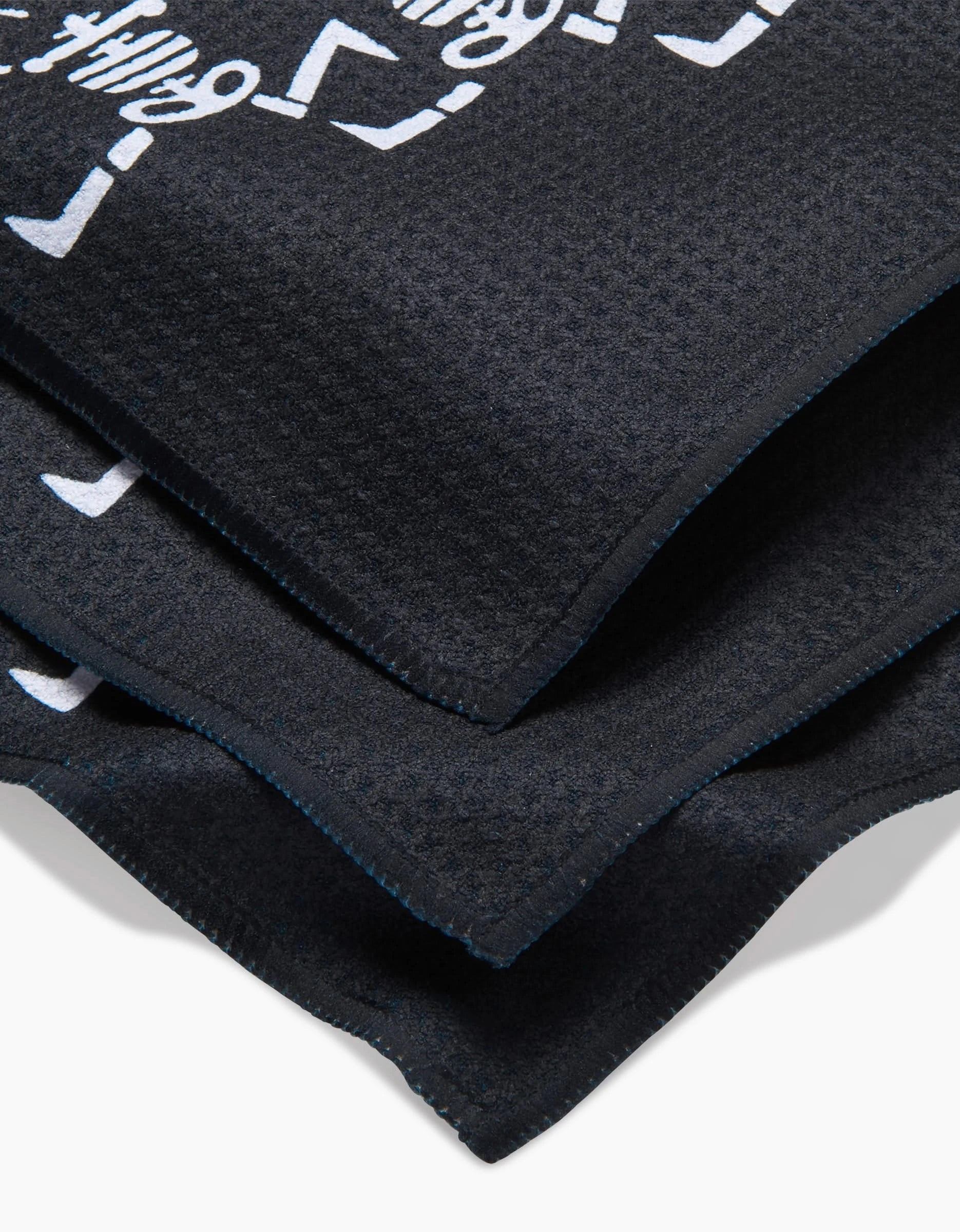 A close-up of two folded black Graveyard Smash fabrics by Carly Berry, featuring recycled materials and partial white graphic designs on the top layer.