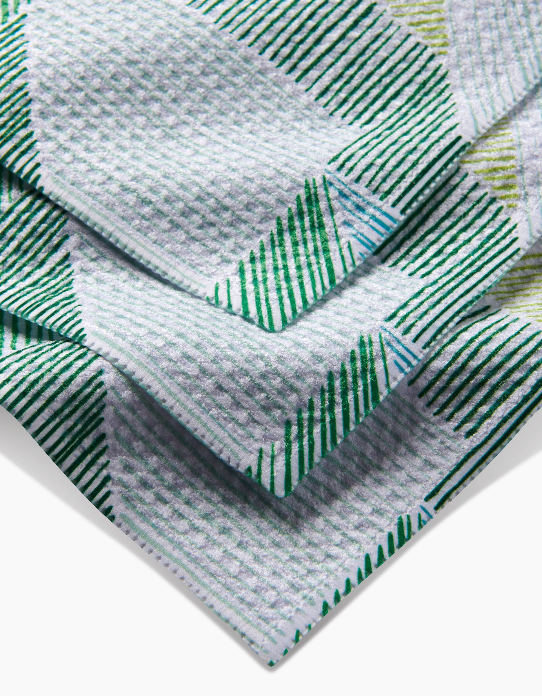 A close-up of the GEOMETRY Green Kites super-absorbent dishcloth, made from recycled materials, featuring a textured fabric with a geometric green, white, and light blue line pattern and a raised grid-like weave.