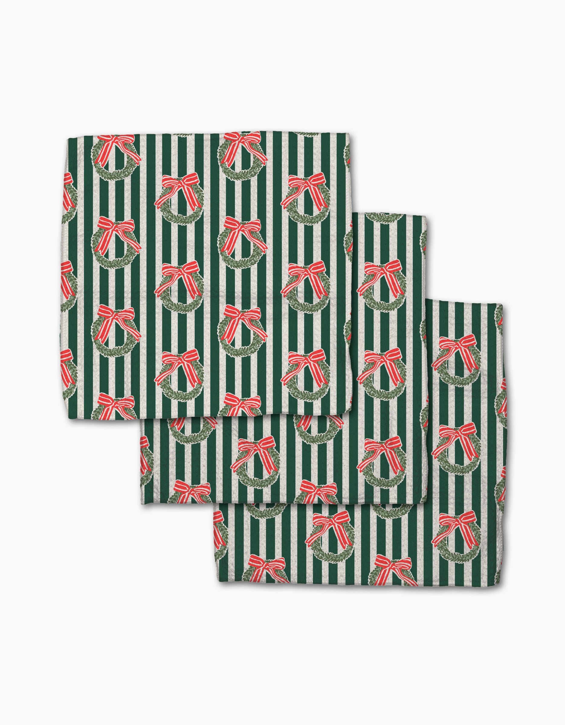 The Green Wreaths dishcloth set by Charlie Rowan Designs features three folded napkins with green and white stripes and red ribbon-tied wreaths, made from recycled materials for a festive touch.