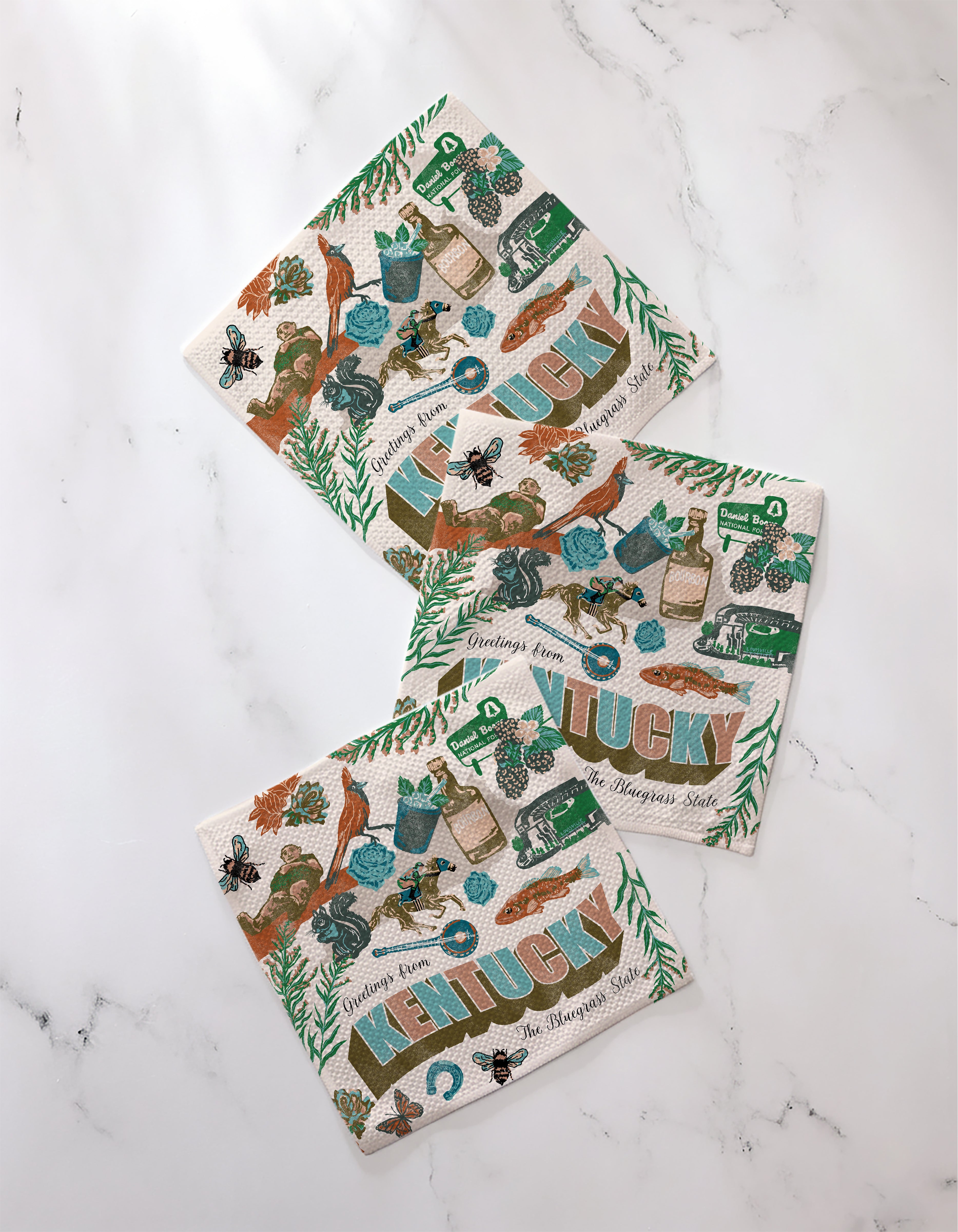 The Geometry "Greetings From Kentucky" set includes three decorative recycled dishcloths with Kentucky-themed illustrations—horses, bourbon, berries, and bold KENTUCKY text—perfect as absorbent kitchen towels.