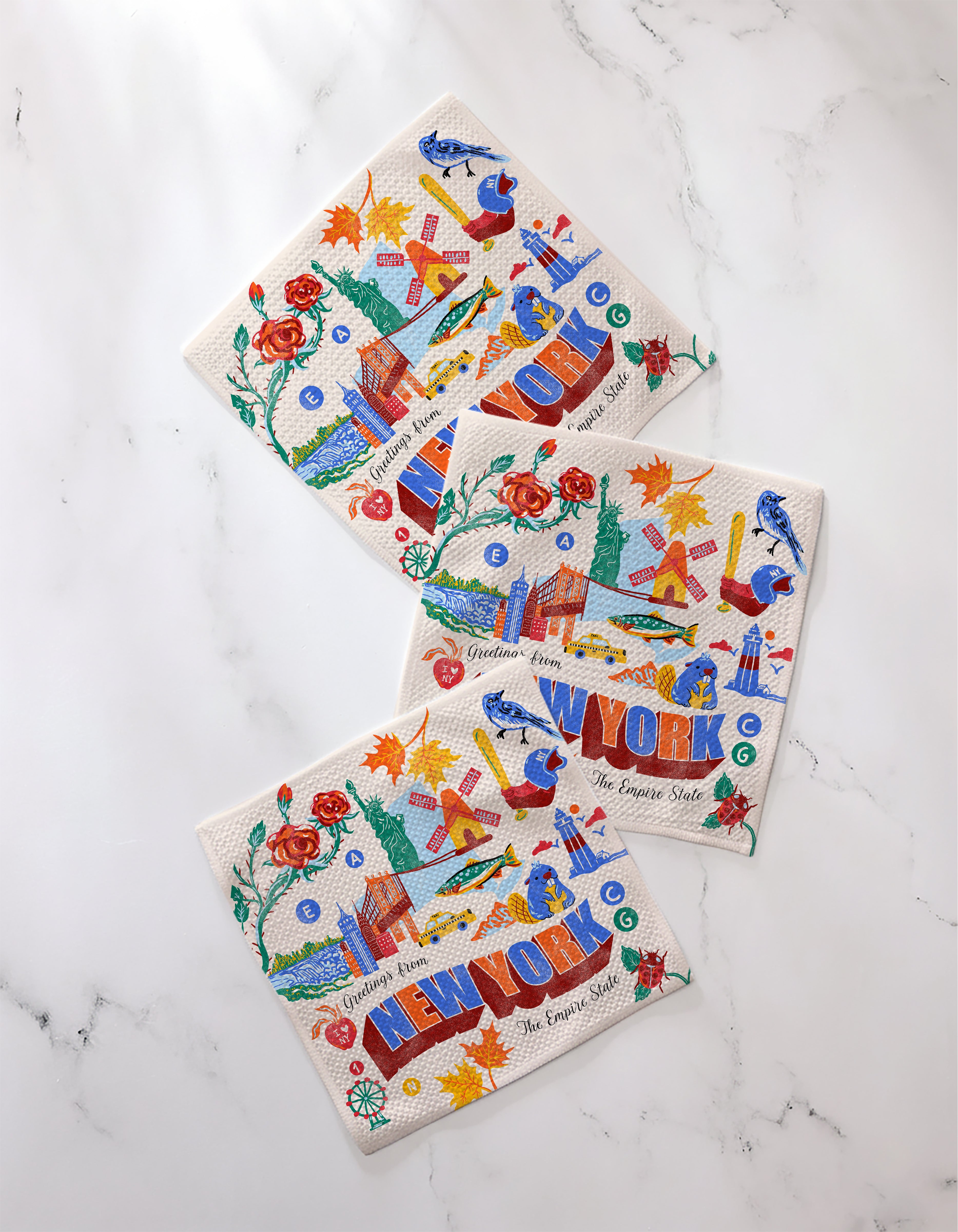 Three "Greetings From New York" paper napkins by Geometry display colorful images like roses, apples, boats, and landmarks—ideal for stylish entertaining and perfectly paired with an absorbent kitchen towel set.