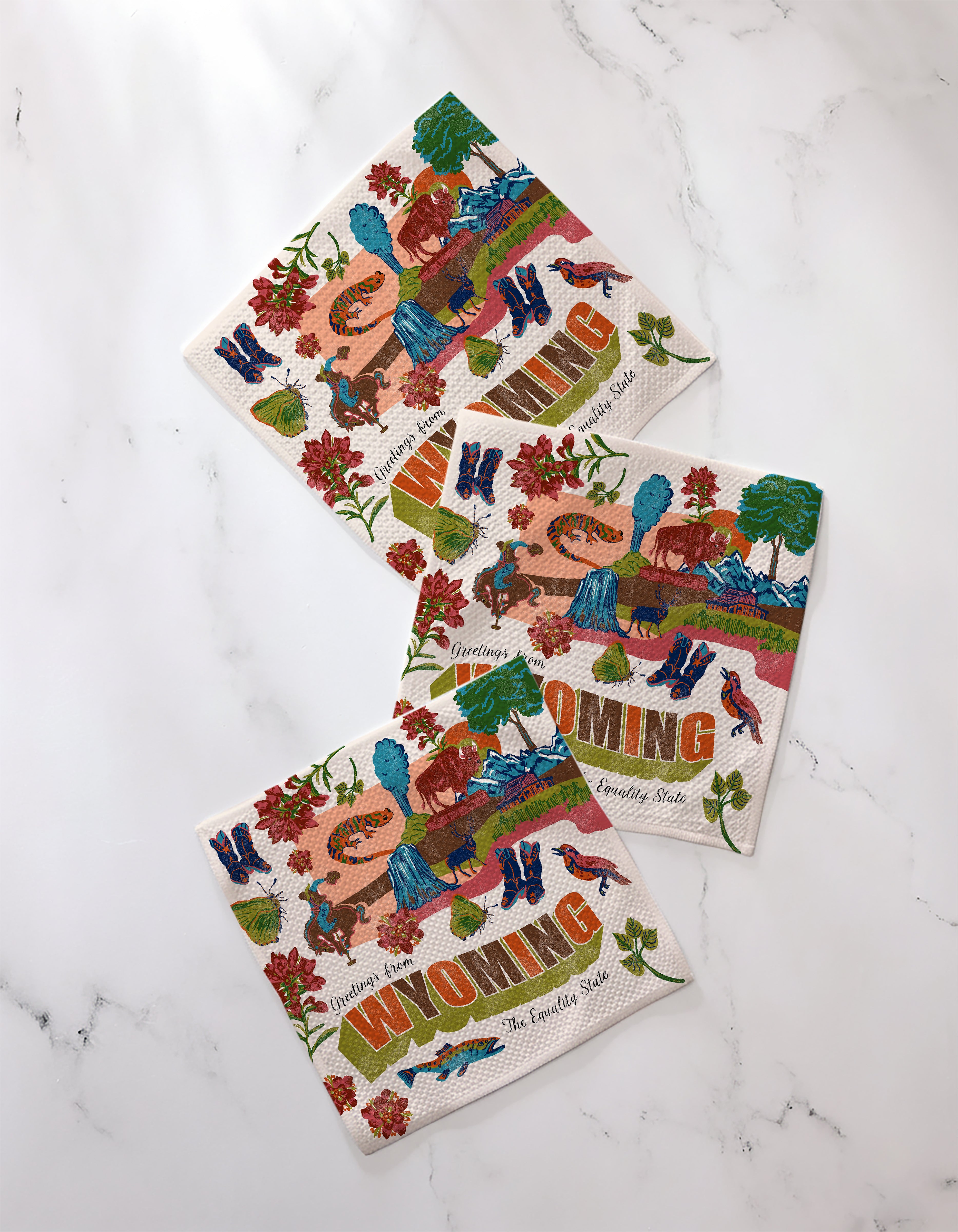 Geometry’s “Greetings From Wyoming” decorative paper napkins display colorful illustrations—cowboy boots, horses, flowers, and “The Equality State”—plus the word WYOMING, made from recycled materials for an eco-friendly touch.