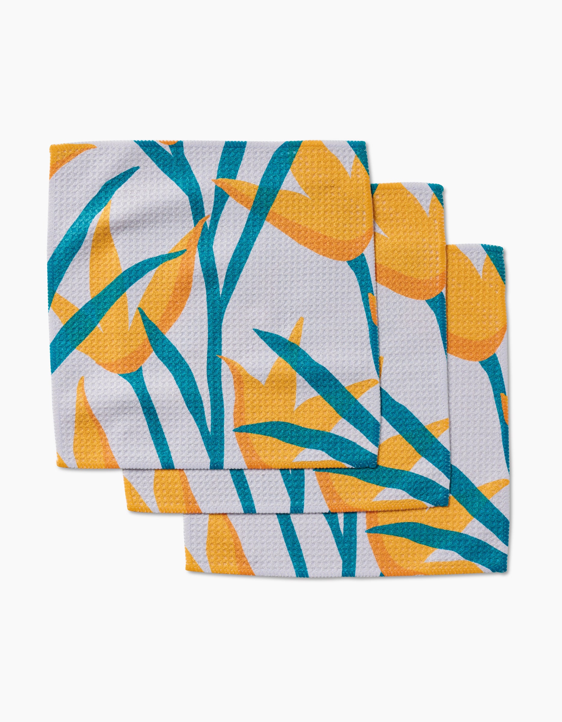 Three GEOMETRY Growth dishcloths with a textured Geoweave surface, each displaying bold yellow tulips and green leaves, are slightly overlapped and arranged on a white background.