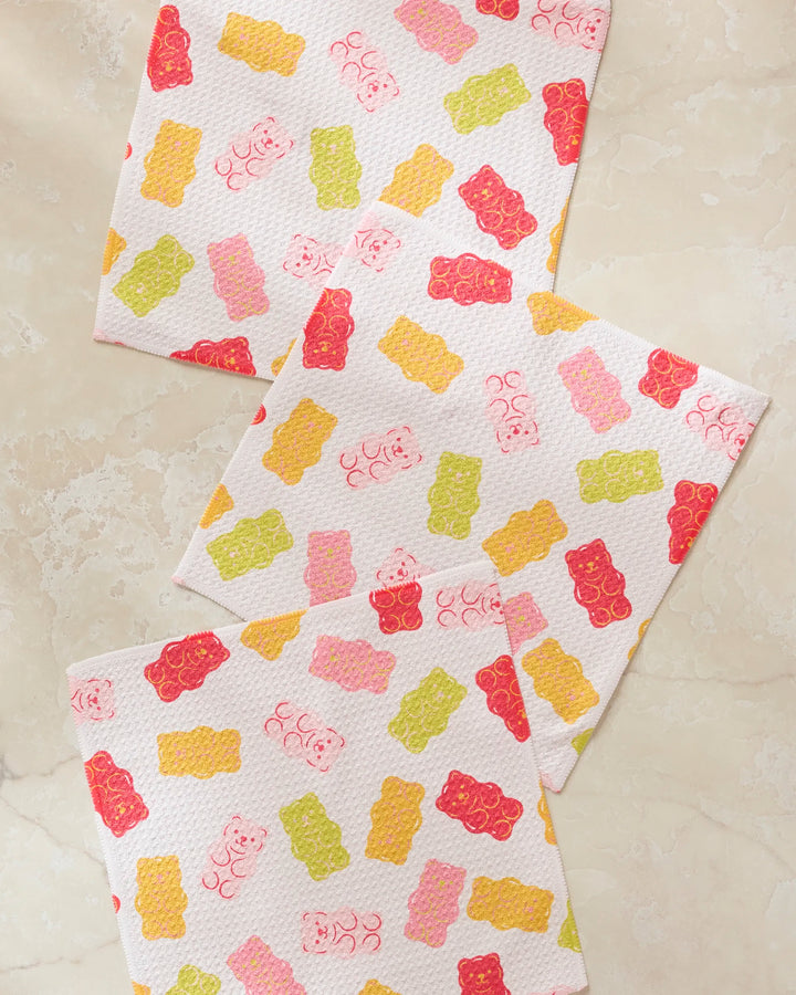 Three white Vaishali Design Studio "Gummy Bear" super-absorbent dishcloths featuring pink, red, yellow, and green gummy bear patterns are displayed on a beige marble surface.