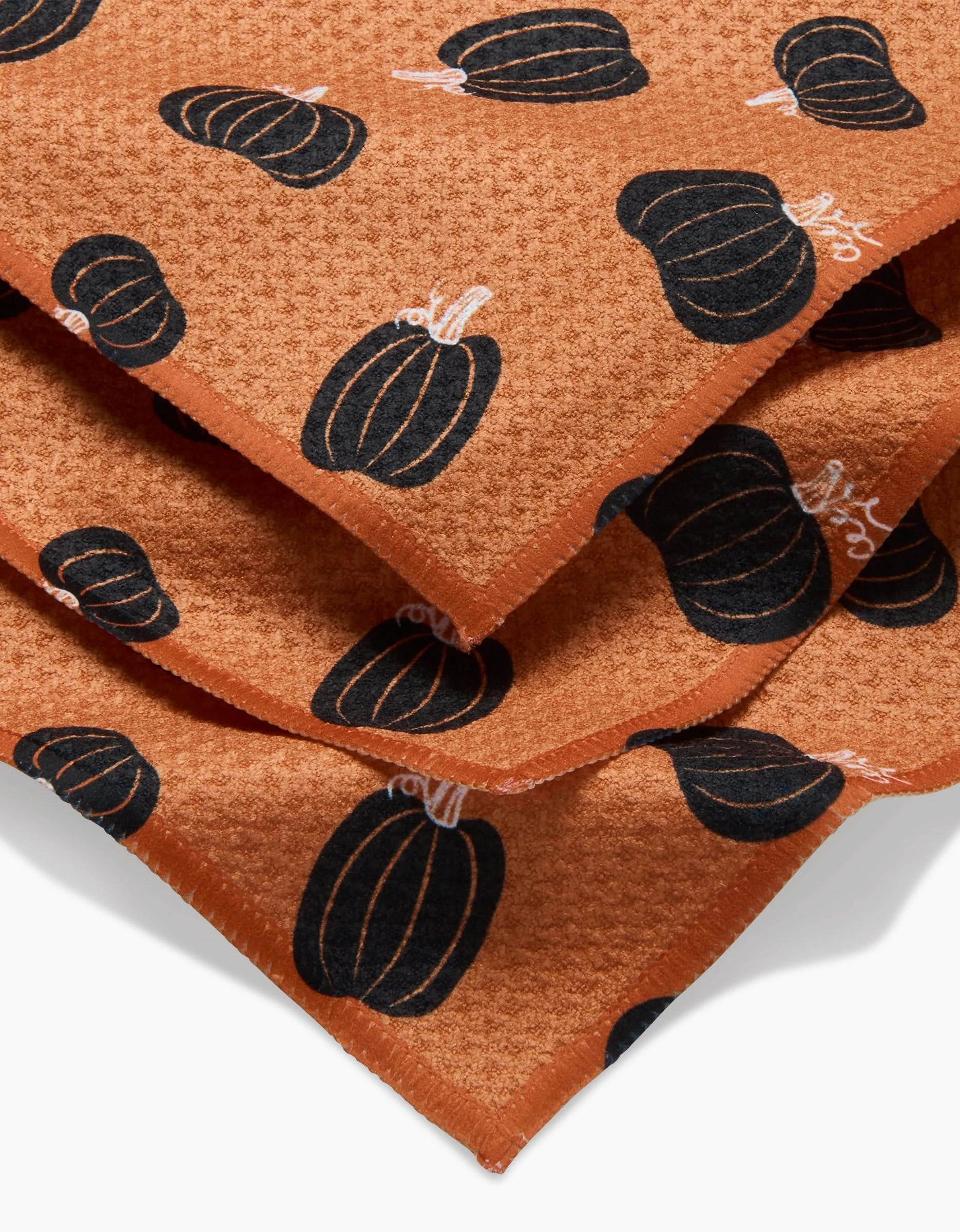 The Hufton Studio Halloween Black Pumpkins dishtowel set features stacked orange fabric with black pumpkin and white stem patterns—super-absorbent, festive, and practical for your kitchen.